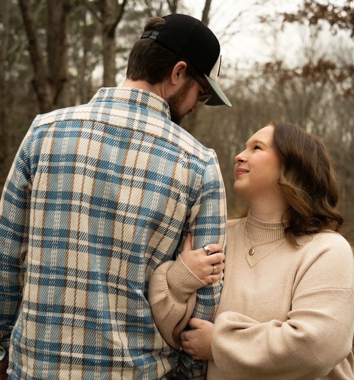 A couple in a plaid shirt and beige sweater share tender romantic moments outdoors during an autumn photoshoot.