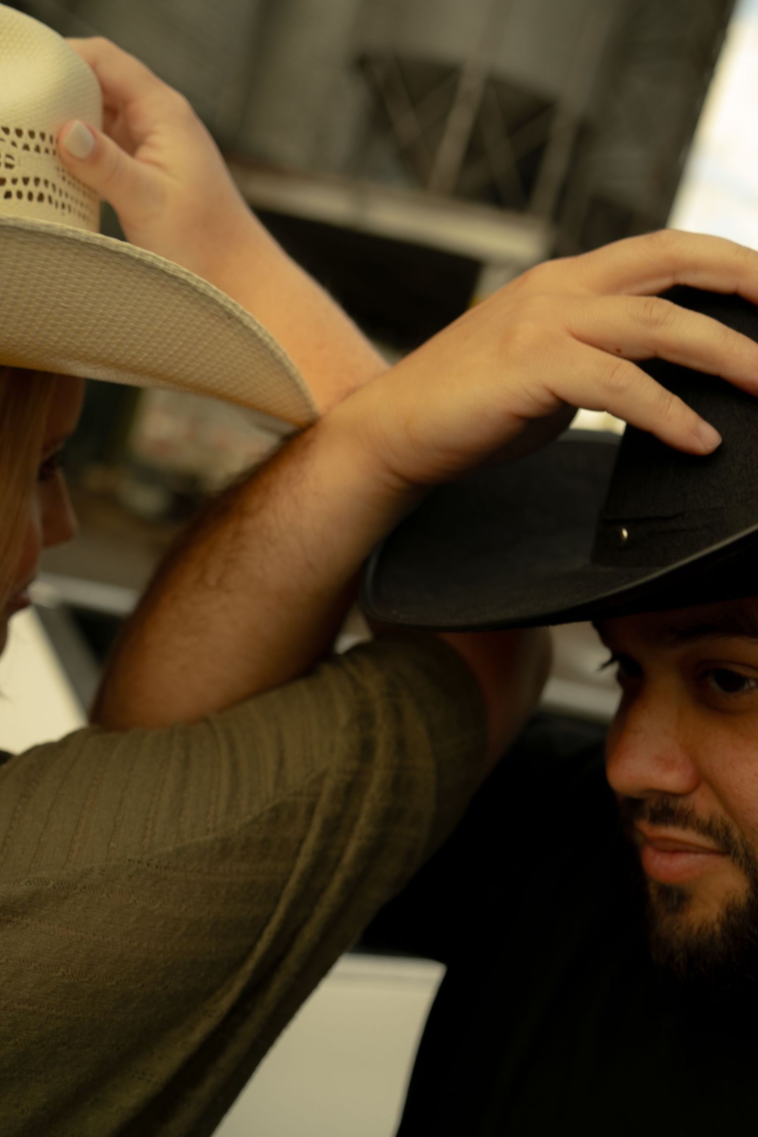 A woman places a dark cowboy hat on a bearded man's head in a hat shop.