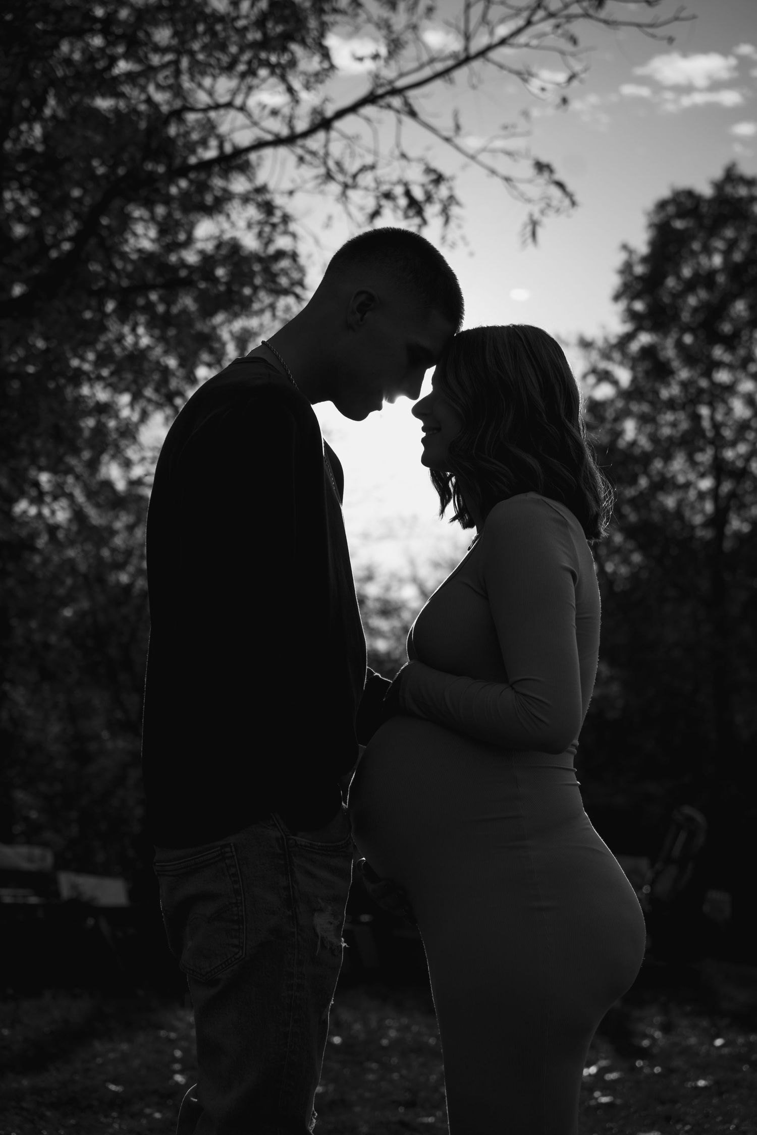 A silhouetted couple shares an intimate moment against a sunset backdrop in a romantic outdoor photo series.