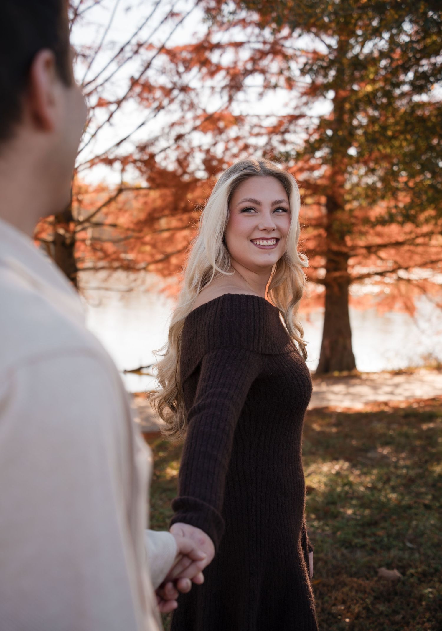 A couple shares an intimate moment in a sunlit autumn forest with golden leaves overhead.