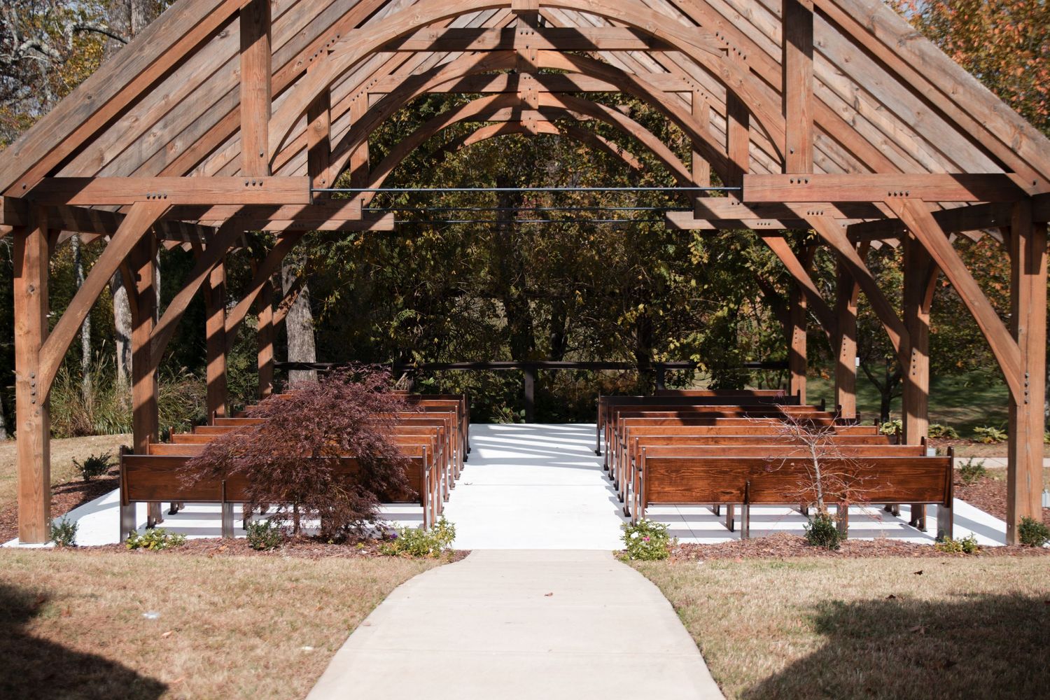 Rustic wooden pavilion with exposed beams and white benches arranged for an outdoor wedding ceremony.
