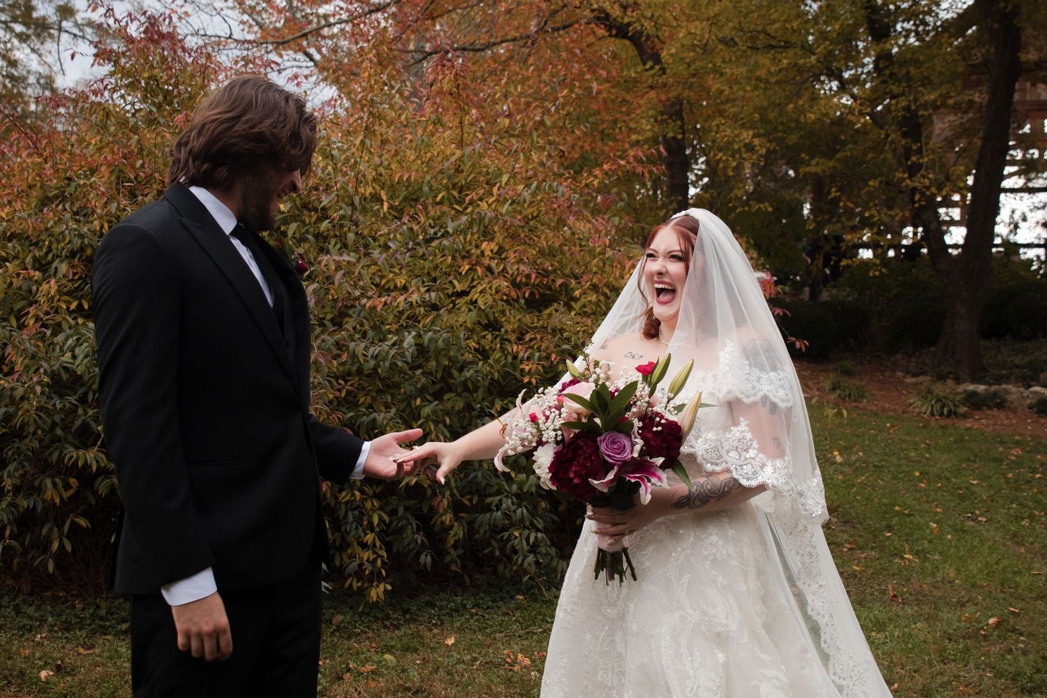 A wedding couple walks together through a scenic autumn park with vibrant fall foliage in the background.