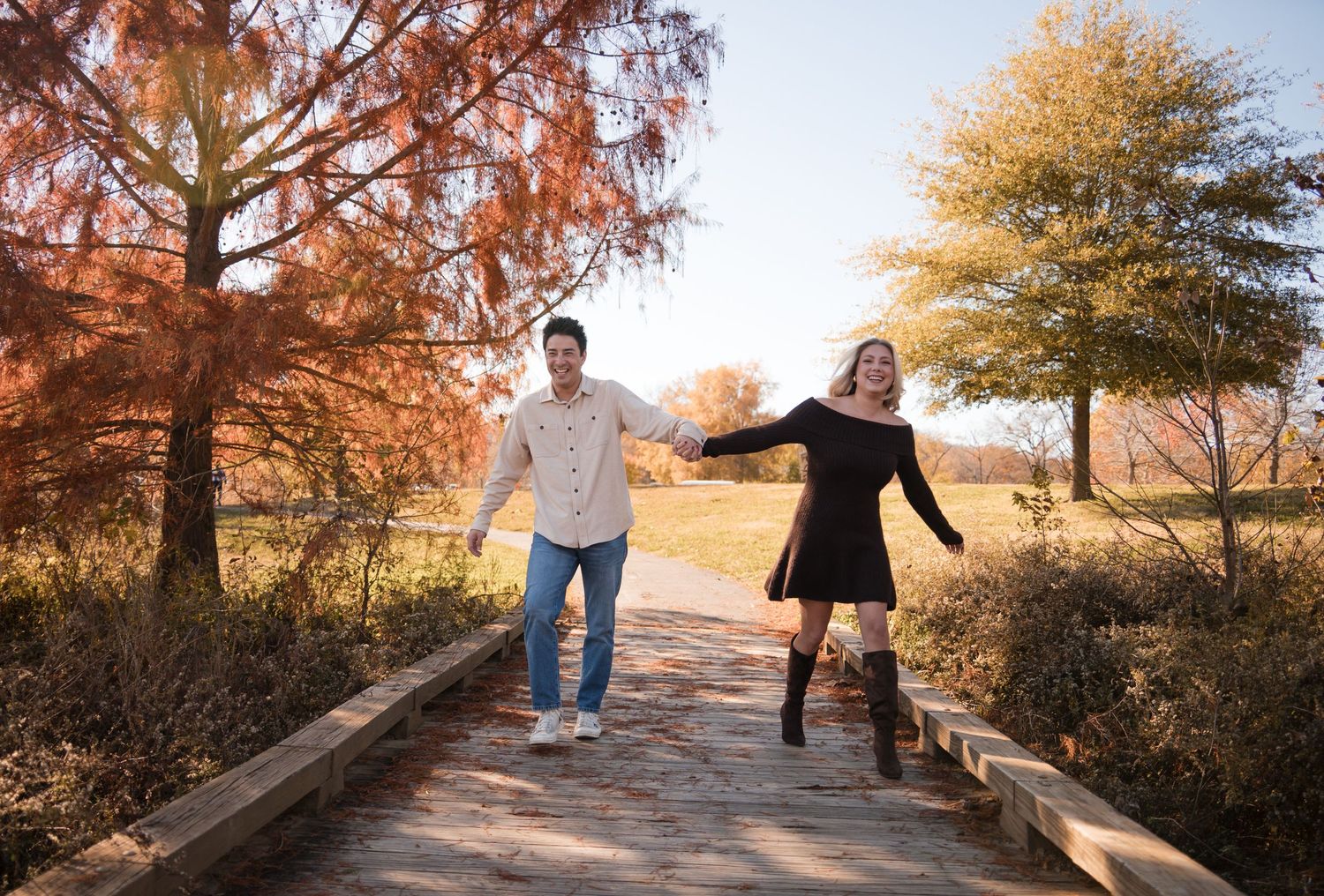 A couple walking together on a wooden bridge during autumn with golden trees in the background.