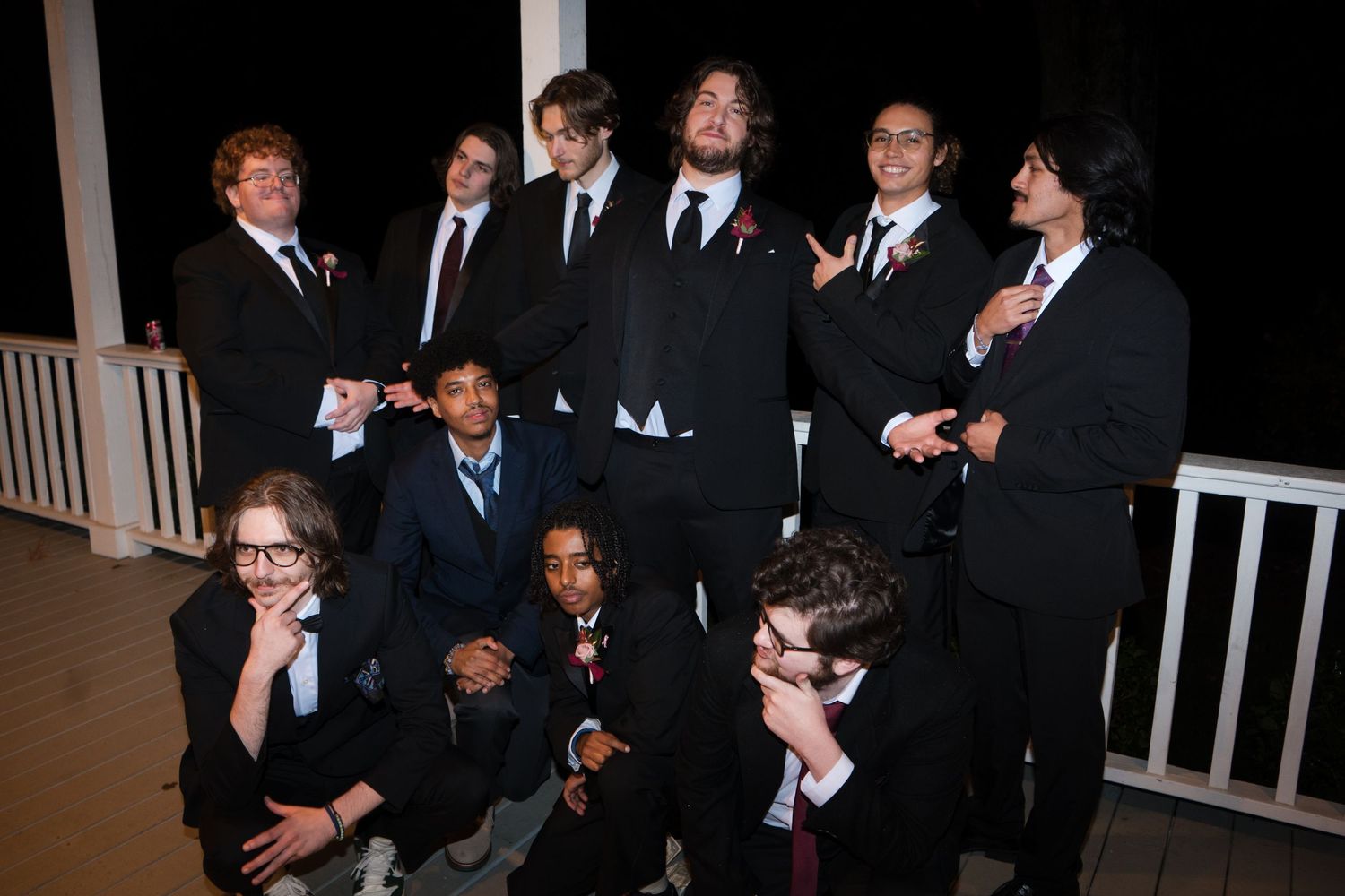 A group of formally dressed people in black tuxedos and suits stand together laughing at an event.