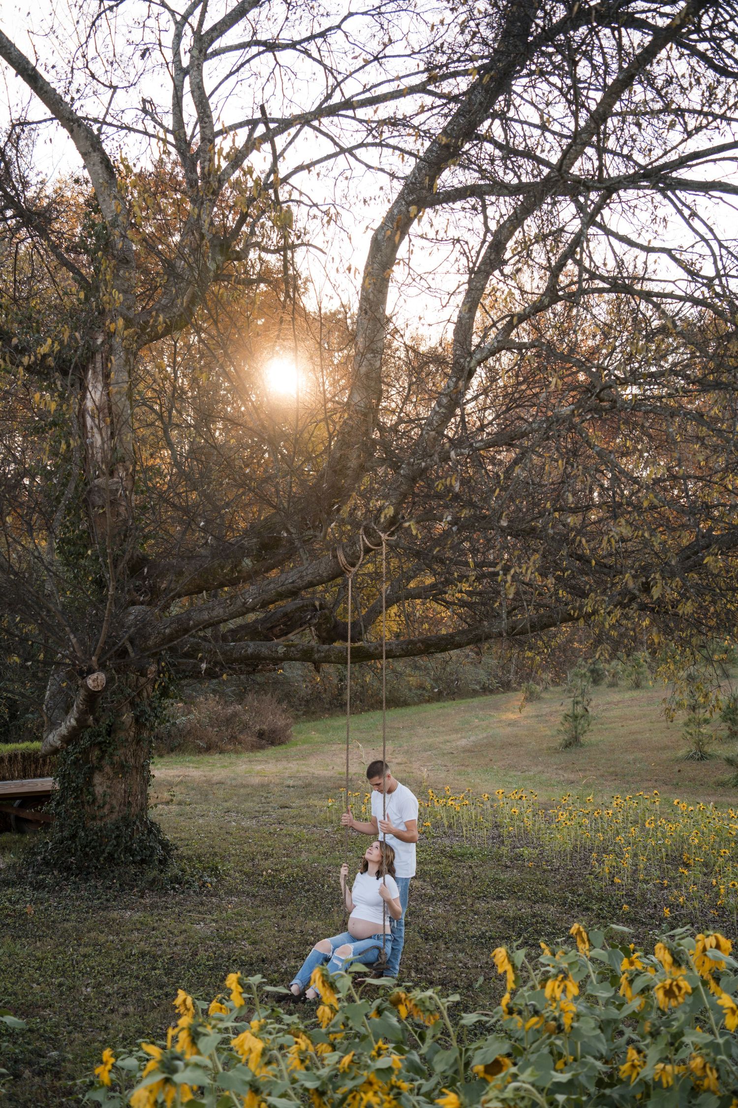 Couple shares a romantic moment at sunset in a field of yellow wildflowers beneath towering autumn trees.