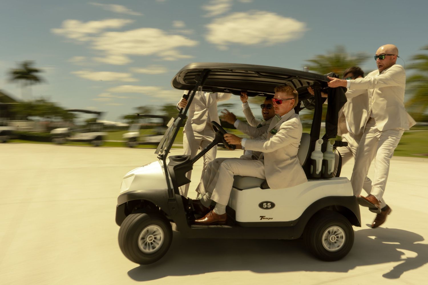 Three men in white suits riding a golf cart at high speed on a sunny day.
