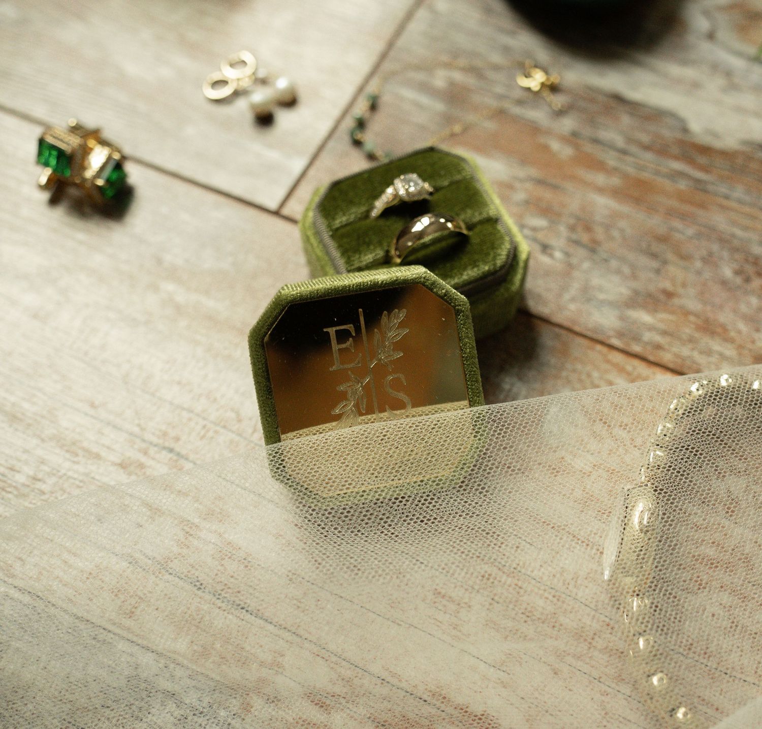 Green velvet octagonal ring box with monogram engraving, displaying a diamond ring on a rustic wood surface.
