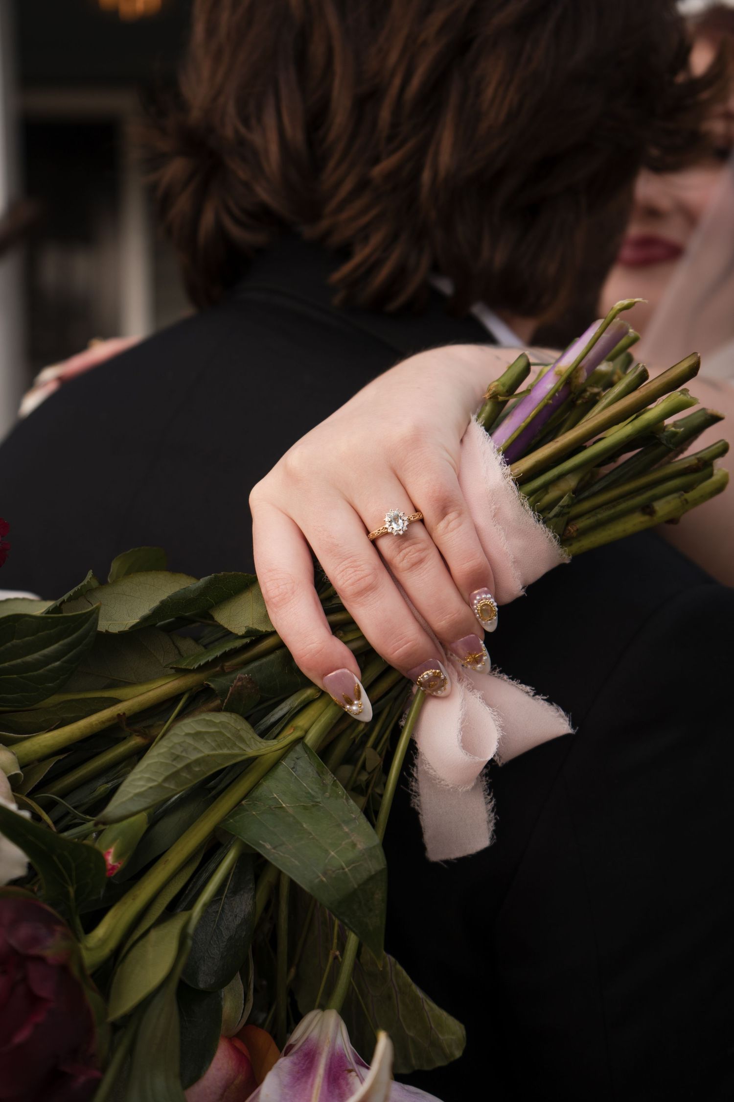 Close-up of hands holding a bouquet of flowers with an engagement ring visible.