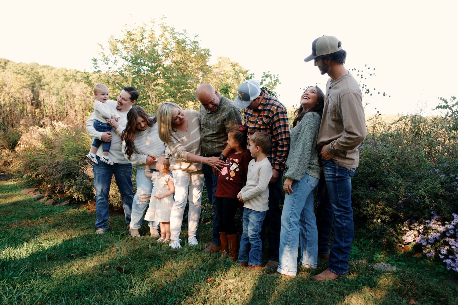 Group gathers outdoors for casual wedding photos in autumn setting with trees.