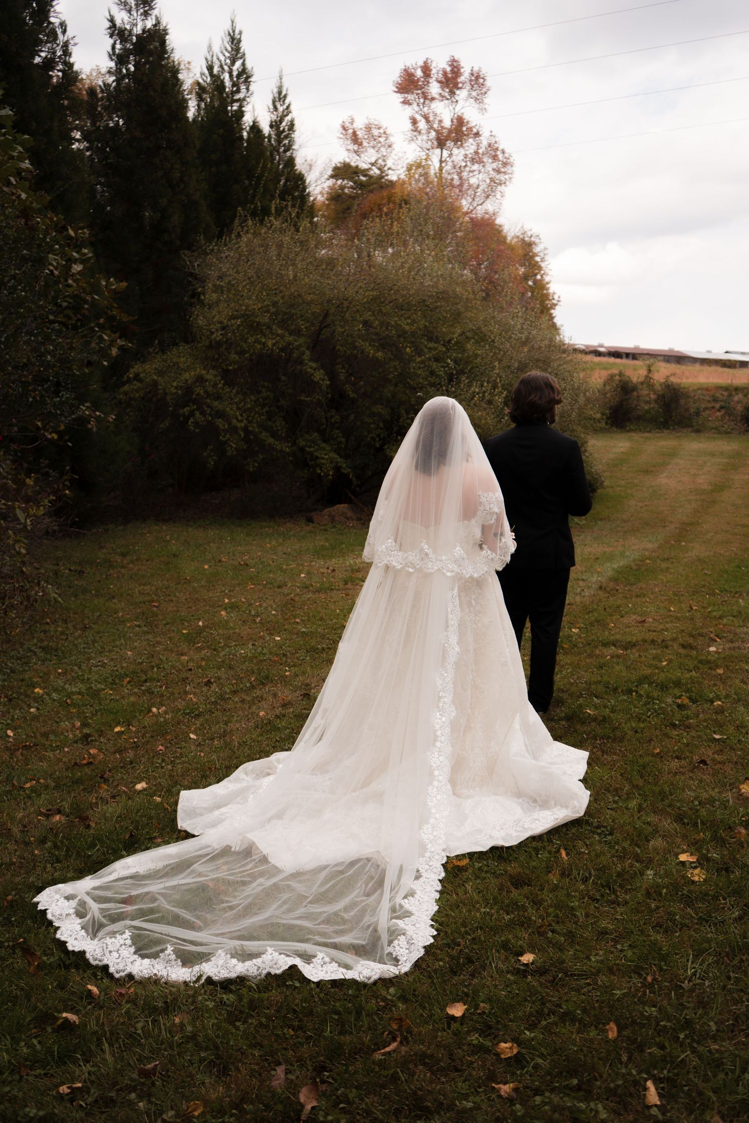 A flowing white wedding dress train with lace details trails across autumn grass.