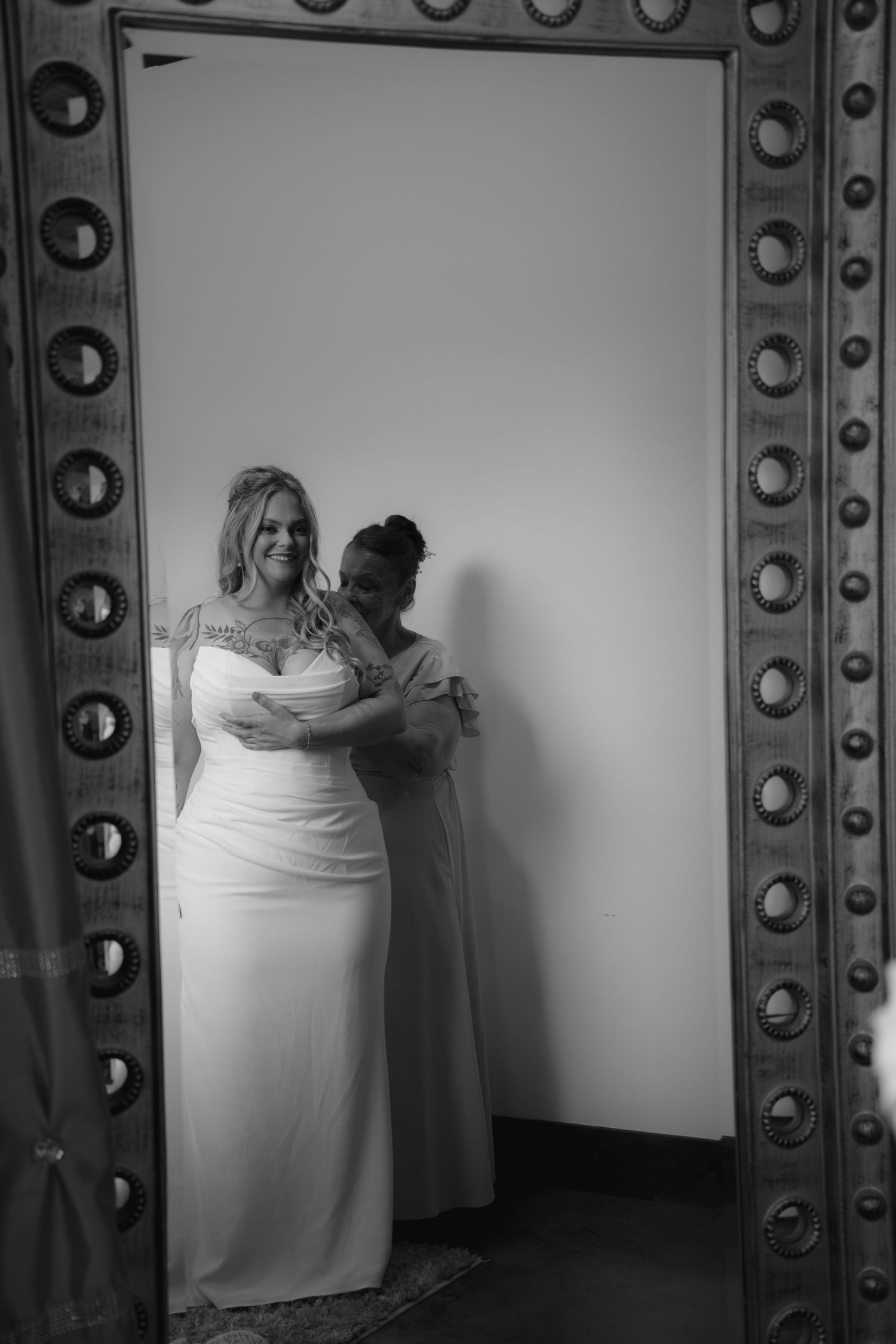 Black and white photo of a bride in a white gown being embraced by a bridesmaid, framed by an ornate doorway.