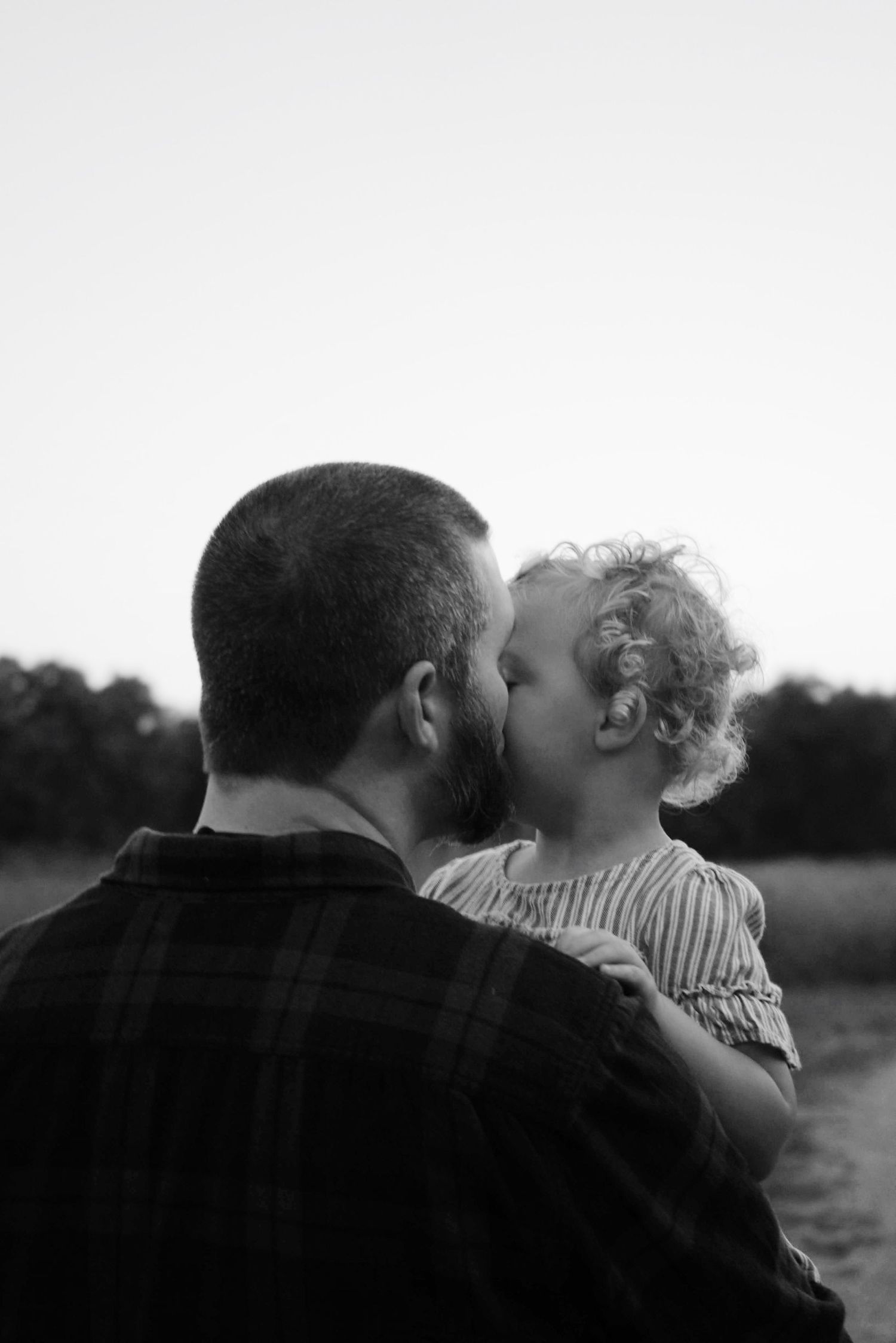 A sequence of black and white photos showing tender moments between a parent and child in a natural outdoor setting.