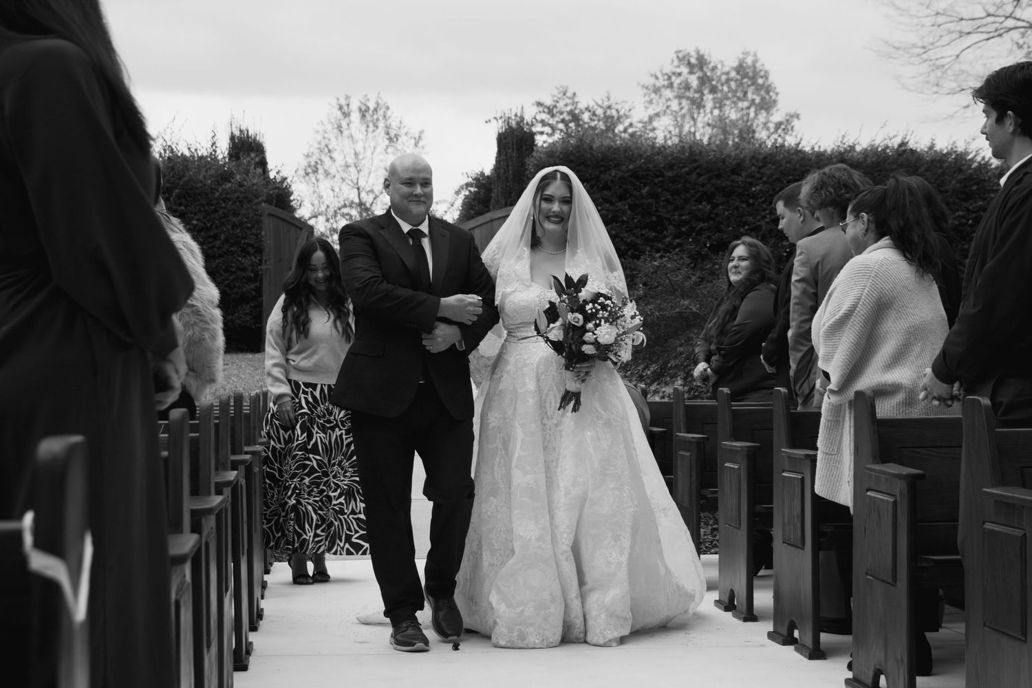 Wedding ceremony procession walking down church aisle with pews and decorations visible.