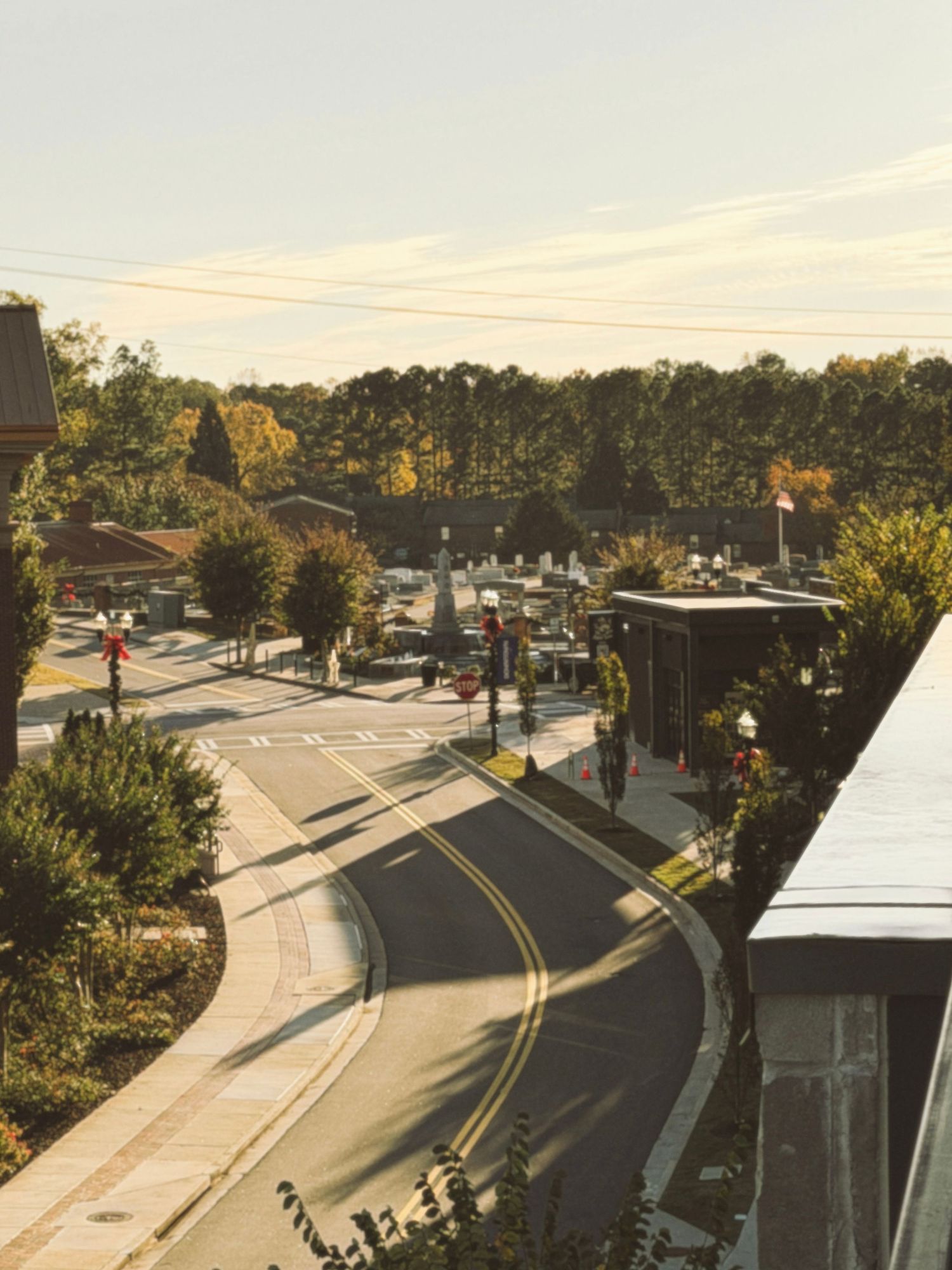 Aerial view of a curved road in a suburban area with parking lots and trees during golden hour lighting.