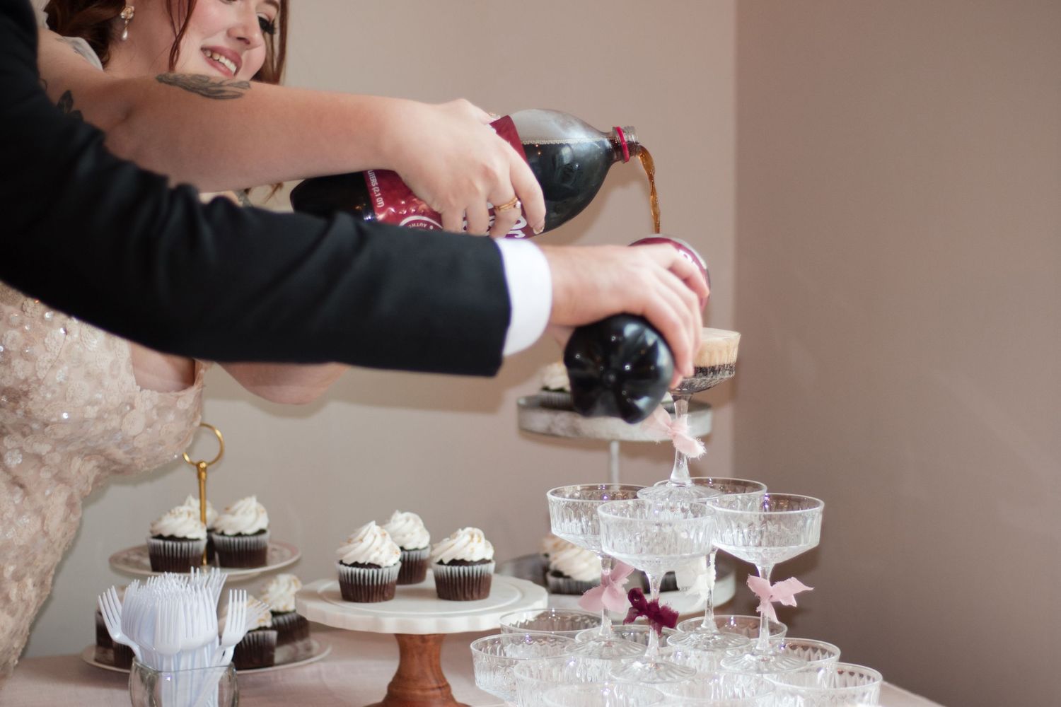 Hands pour champagne into glasses at an elegant wedding reception with tiered dessert displays and cake stands.