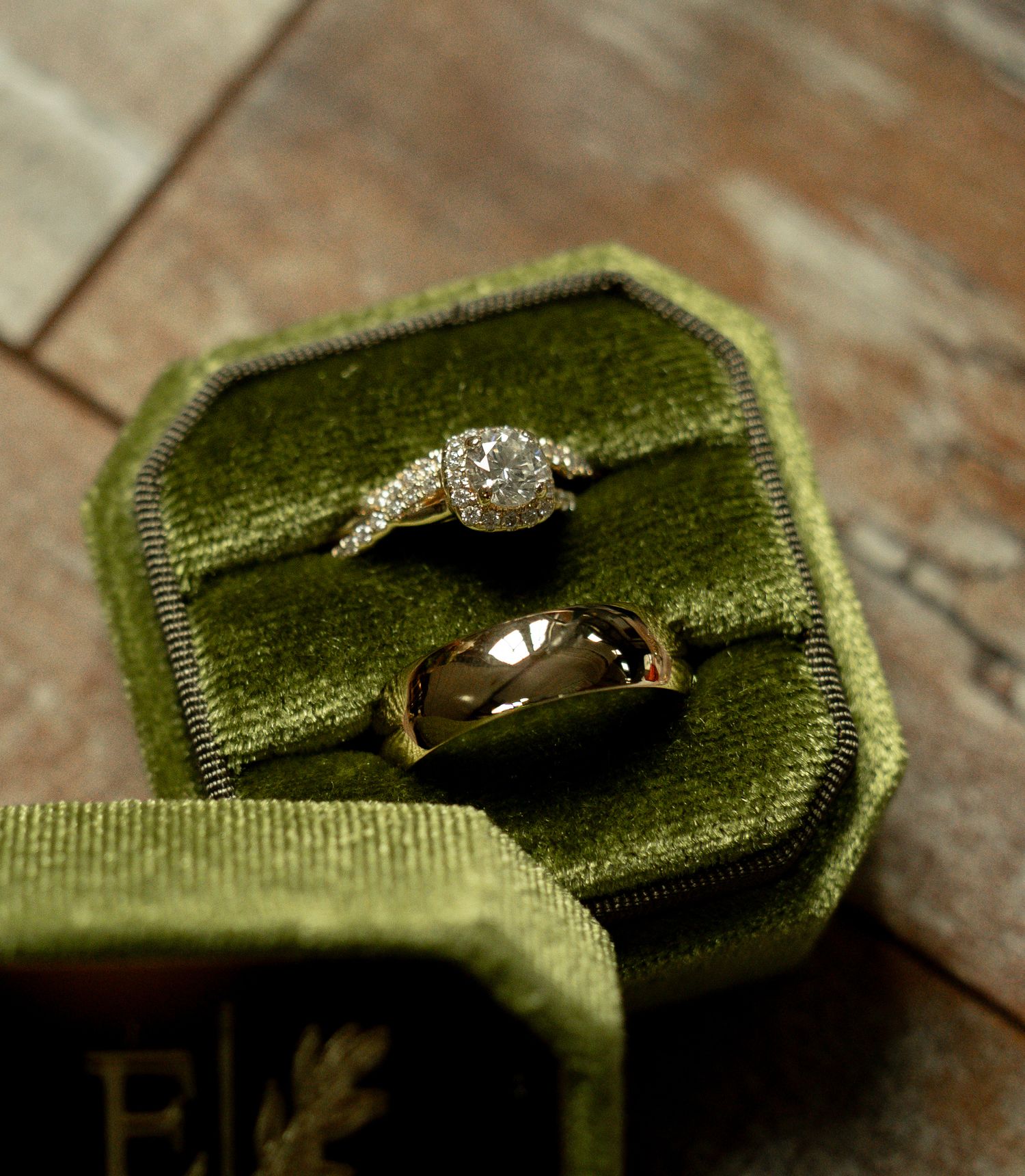 Two elegant rings in a green velvet octagonal box, featuring a diamond halo engagement ring and a gold band.