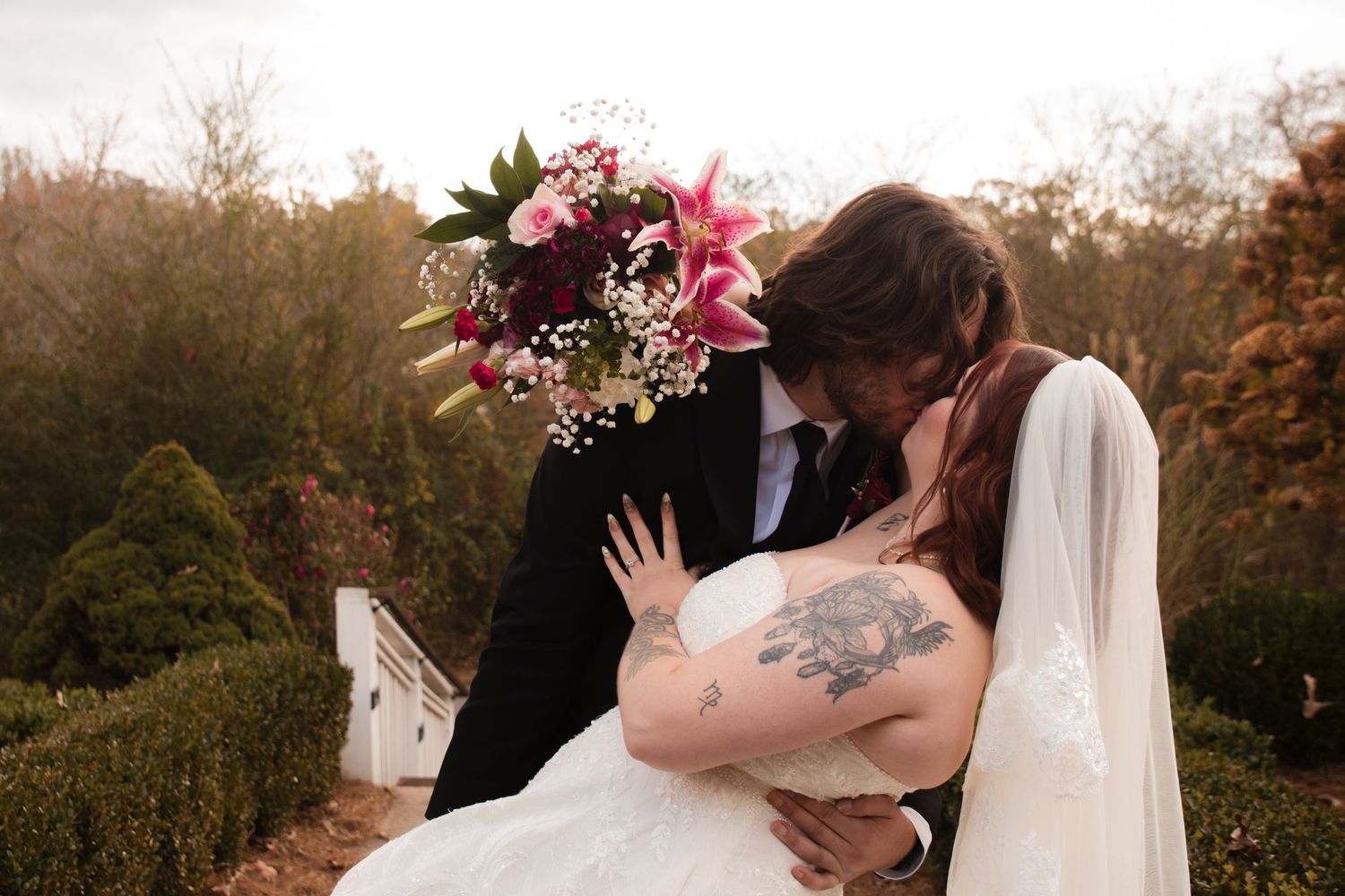 A romantic wedding kiss captured outdoors with fall foliage and a colorful bouquet.