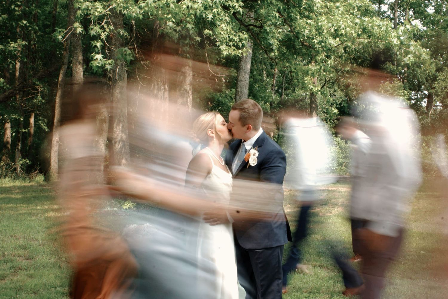Motion blur photograph of newlyweds kissing during an outdoor garden wedding celebration.