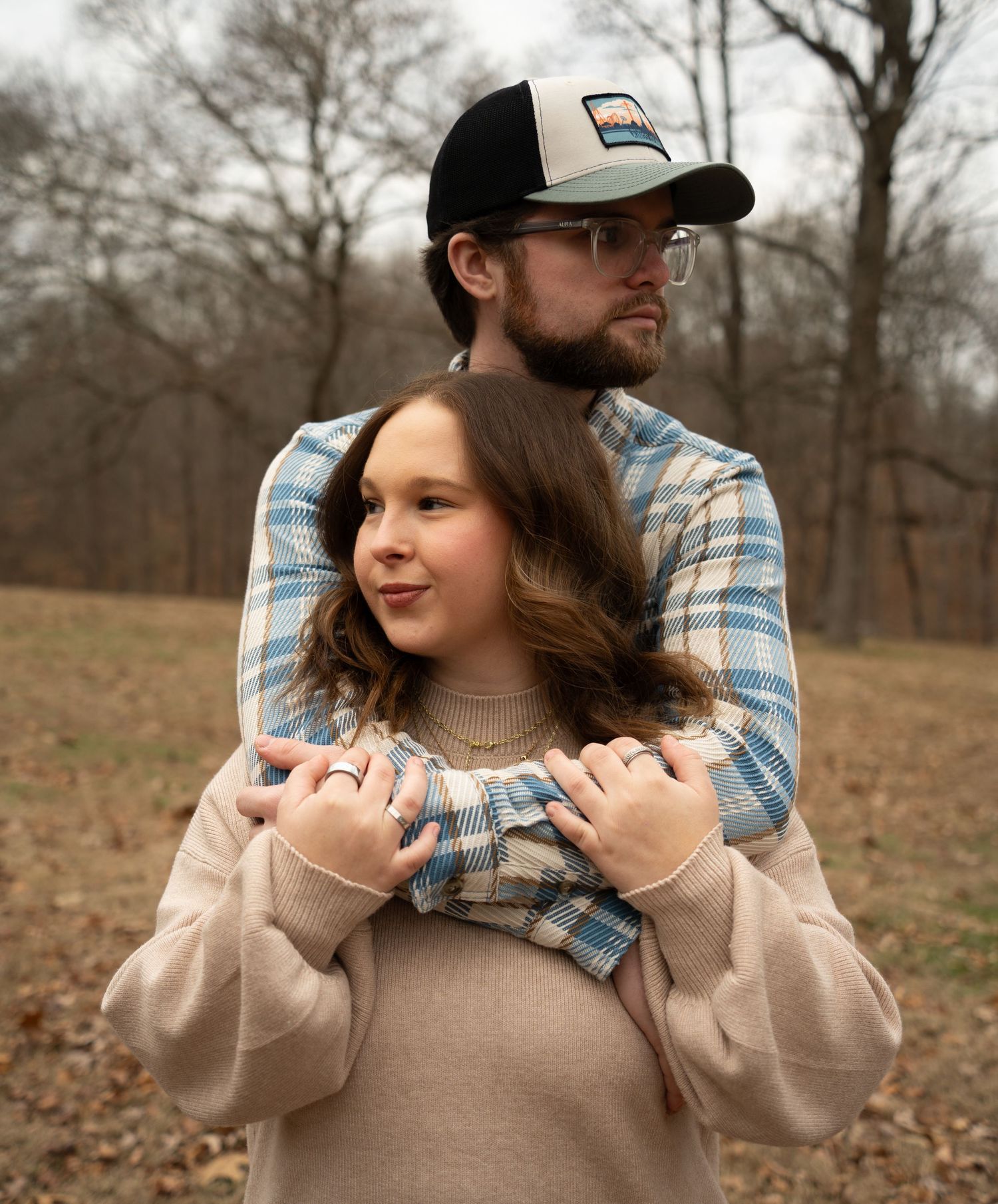 A couple in casual attire shares a tender moment in a natural outdoor setting during autumn.