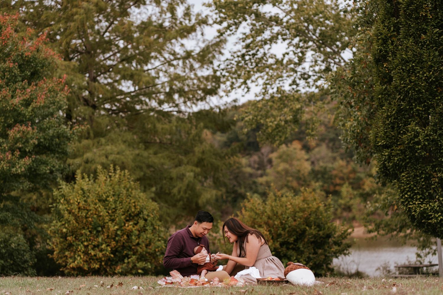 A couple sits together on a blanket having a romantic picnic by a scenic lake on a sunny autumn afternoon.