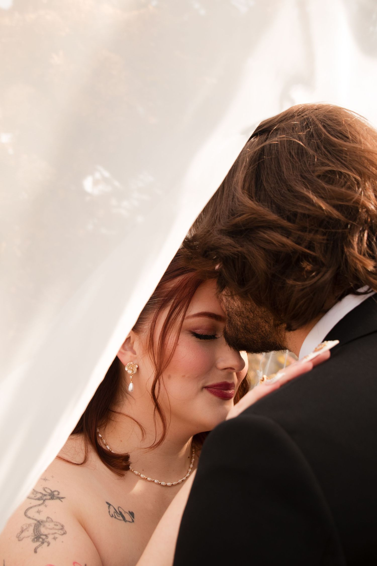 Close-up details of a bride with pearl necklace and visible tattoos in soft lighting.