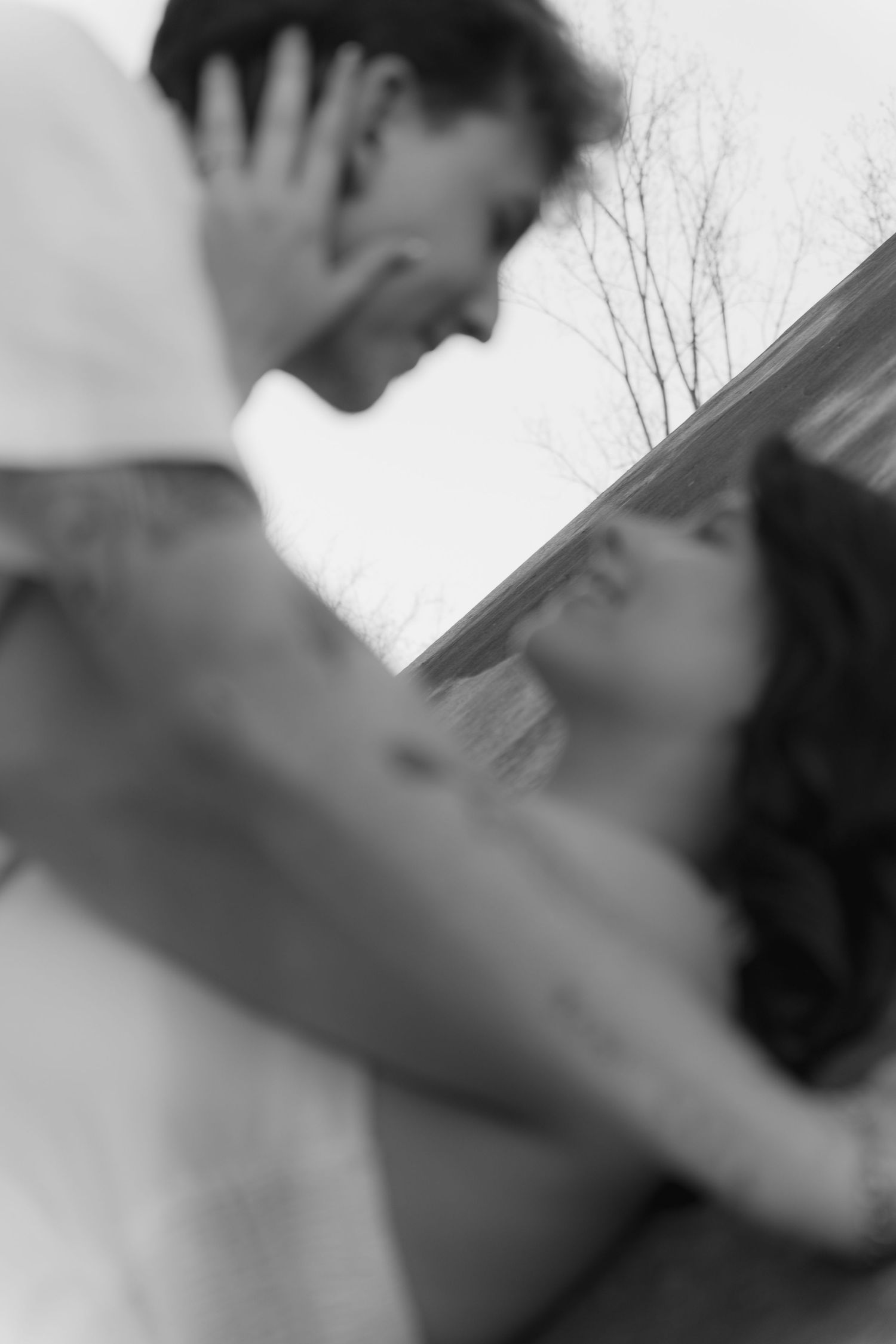 Black and white artistic photo of a couple leaning in for a kiss, captured with a soft focus blur effect outdoors.
