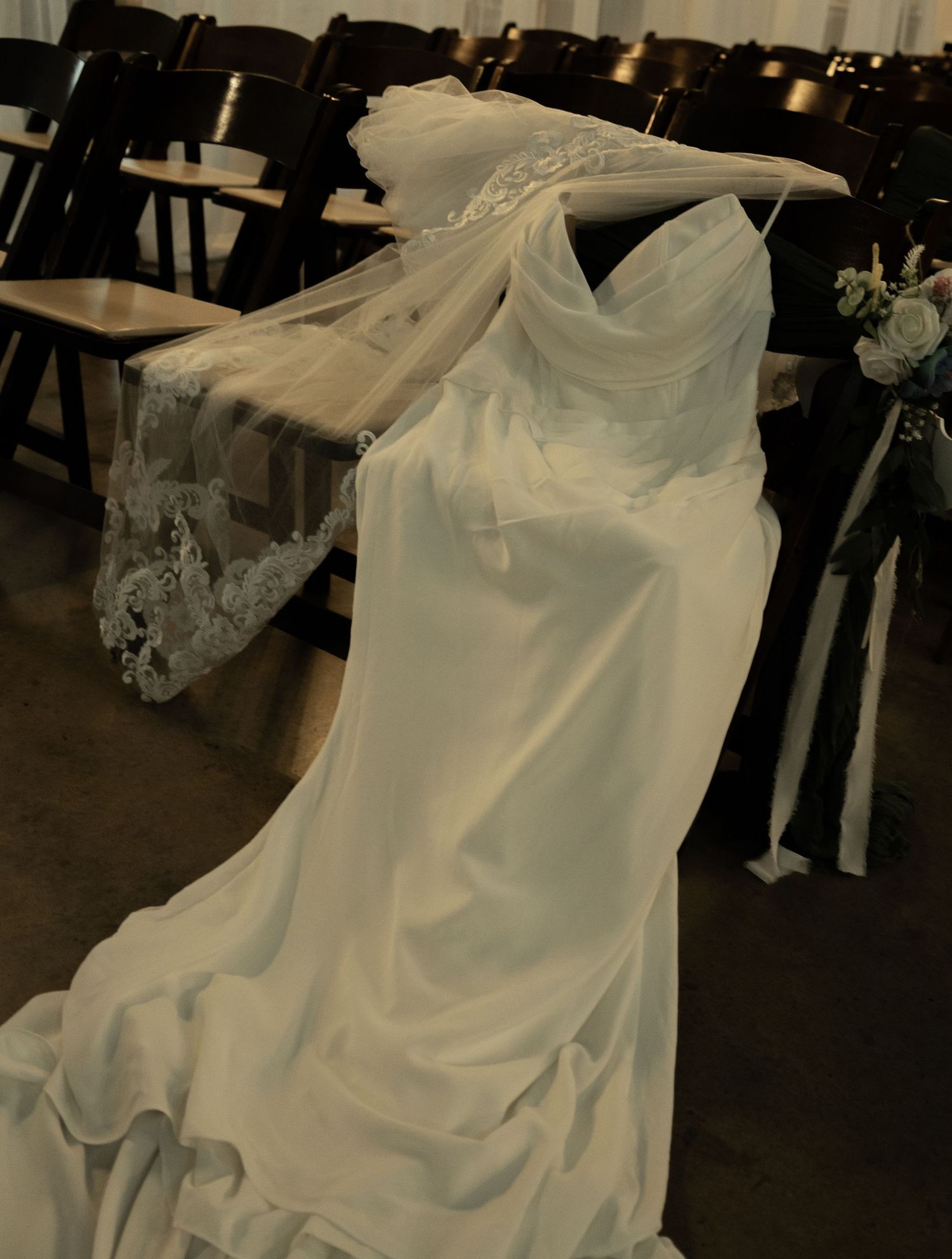 Elegant white wedding dress with lace veil draped over chairs in a wedding venue.
