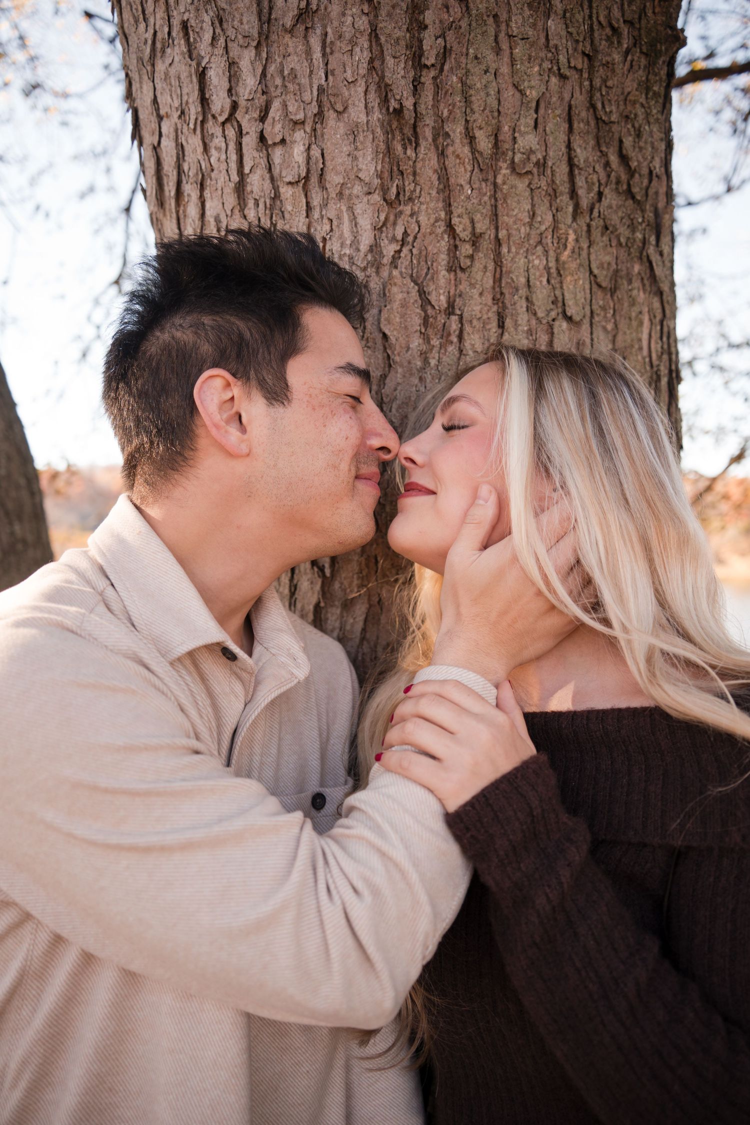 A couple shares a romantic kiss against a tree trunk in a series of connected photos.