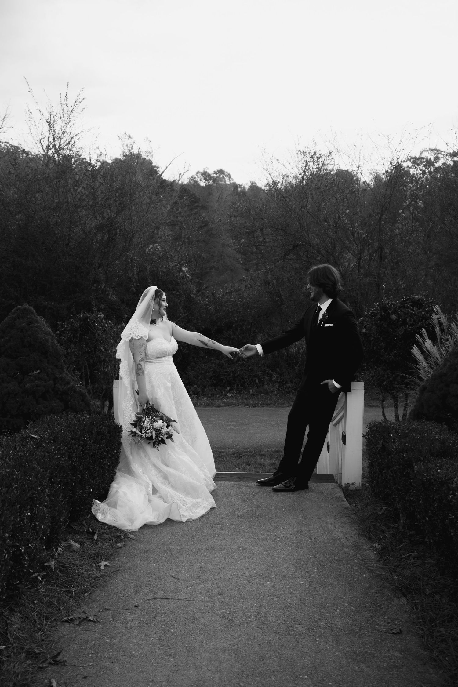 Playful black and white wedding photos showing a couple dancing and twirling on a garden path.