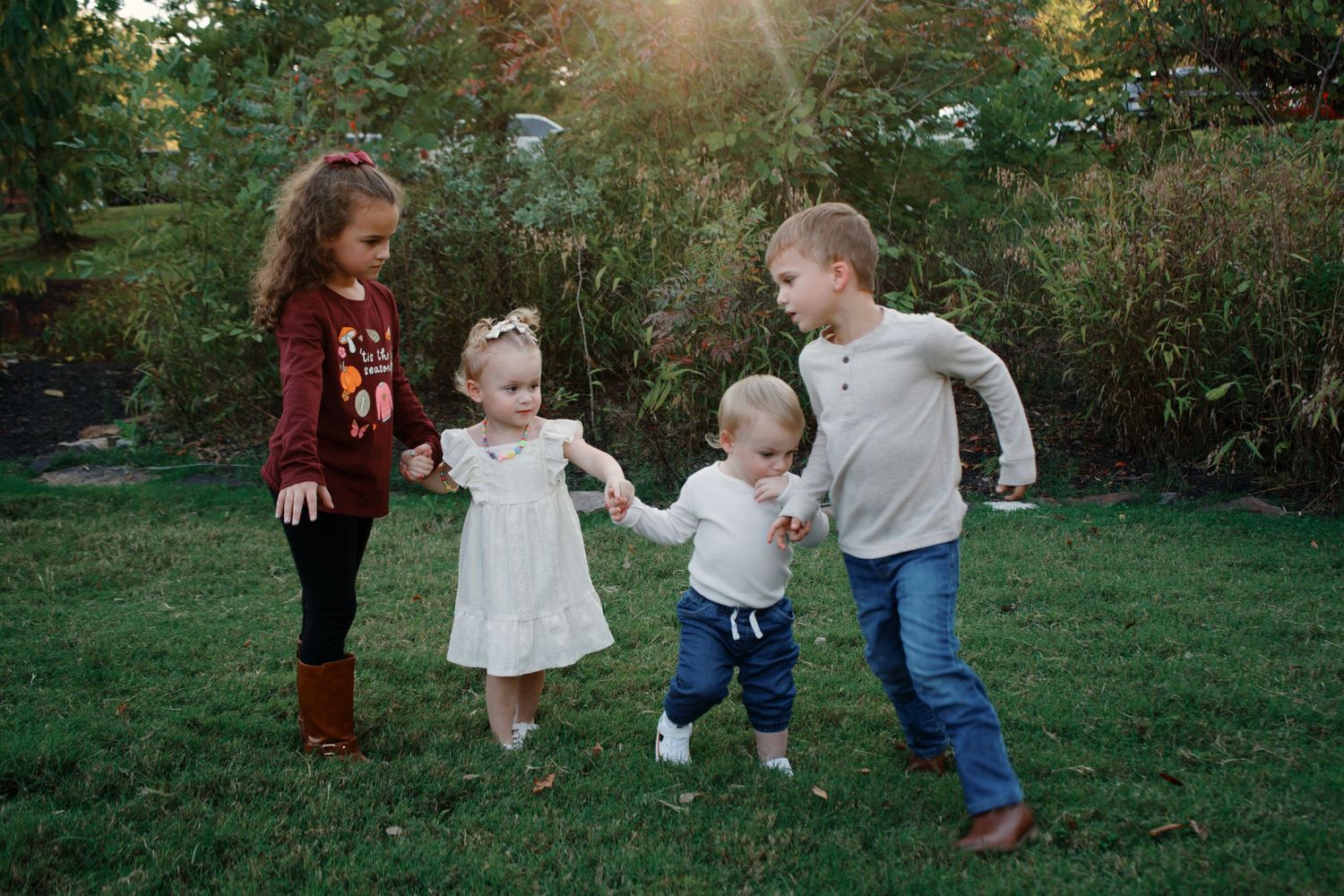 Children play and interact on a grassy lawn surrounded by greenery on a sunny afternoon.