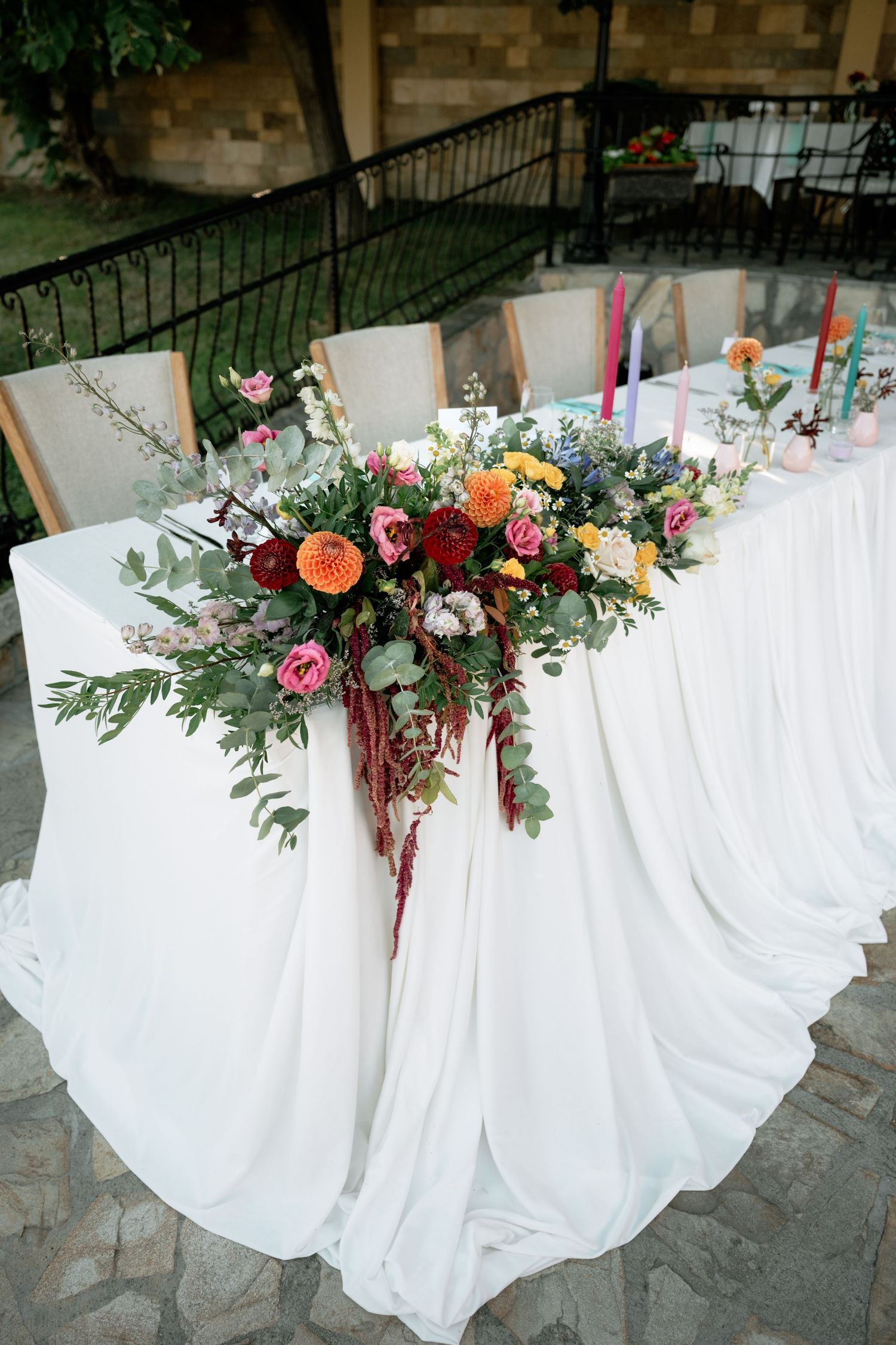 A series of wedding reception tables decorated with flowing white tablecloths and colorful floral arrangements with greenery.