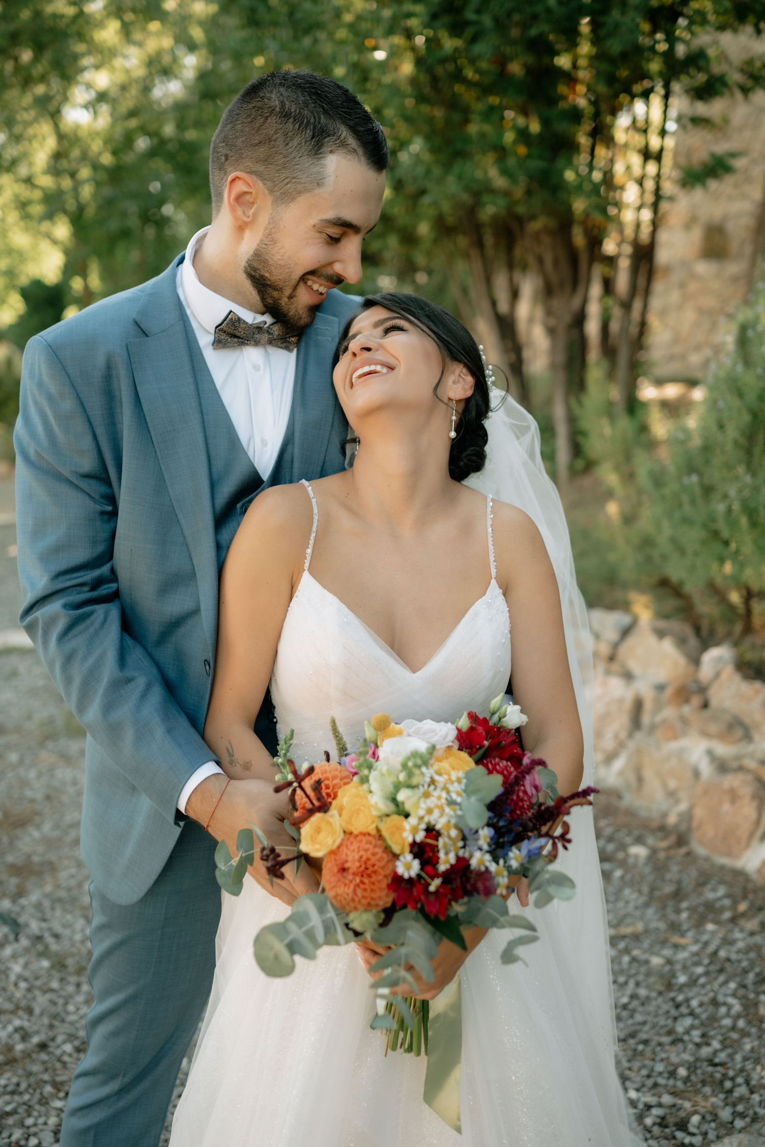 Newlyweds share intimate moments in a wooded outdoor setting with autumn-colored wedding bouquet.