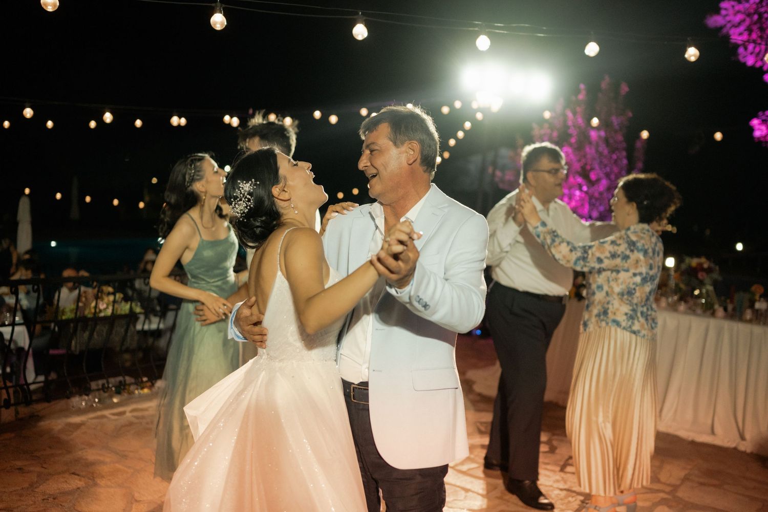 Couples dance together at an outdoor evening wedding reception under string lights and a glowing night sky.