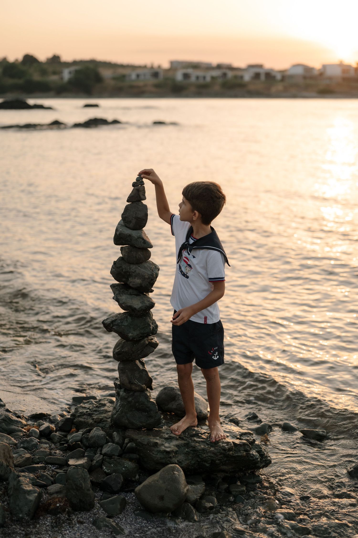 Child stacks rocks along a scenic beach shoreline at sunset creating a peaceful coastal moment.