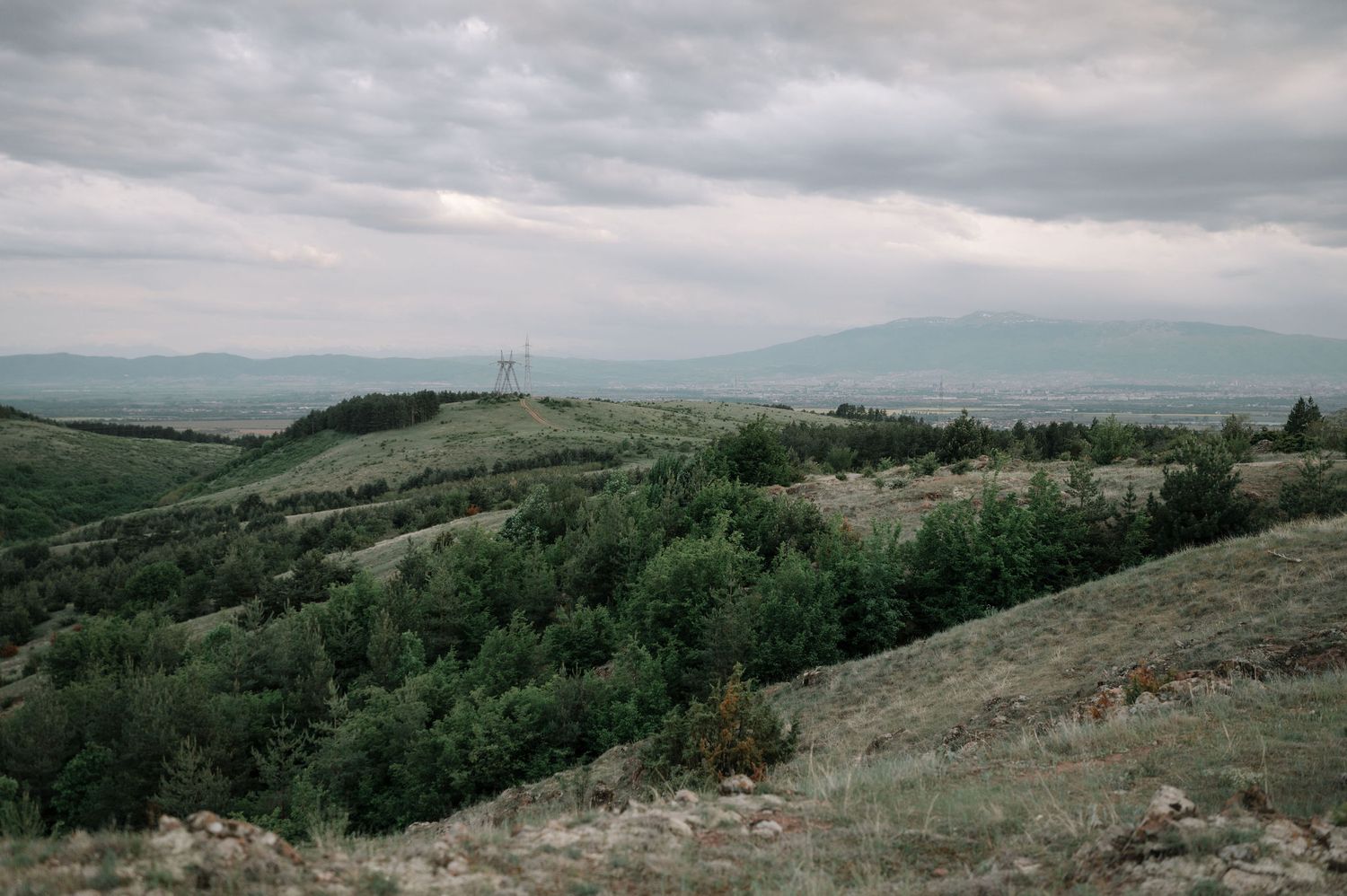 Rolling hills and grasslands stretch across a moody landscape under overcast skies.