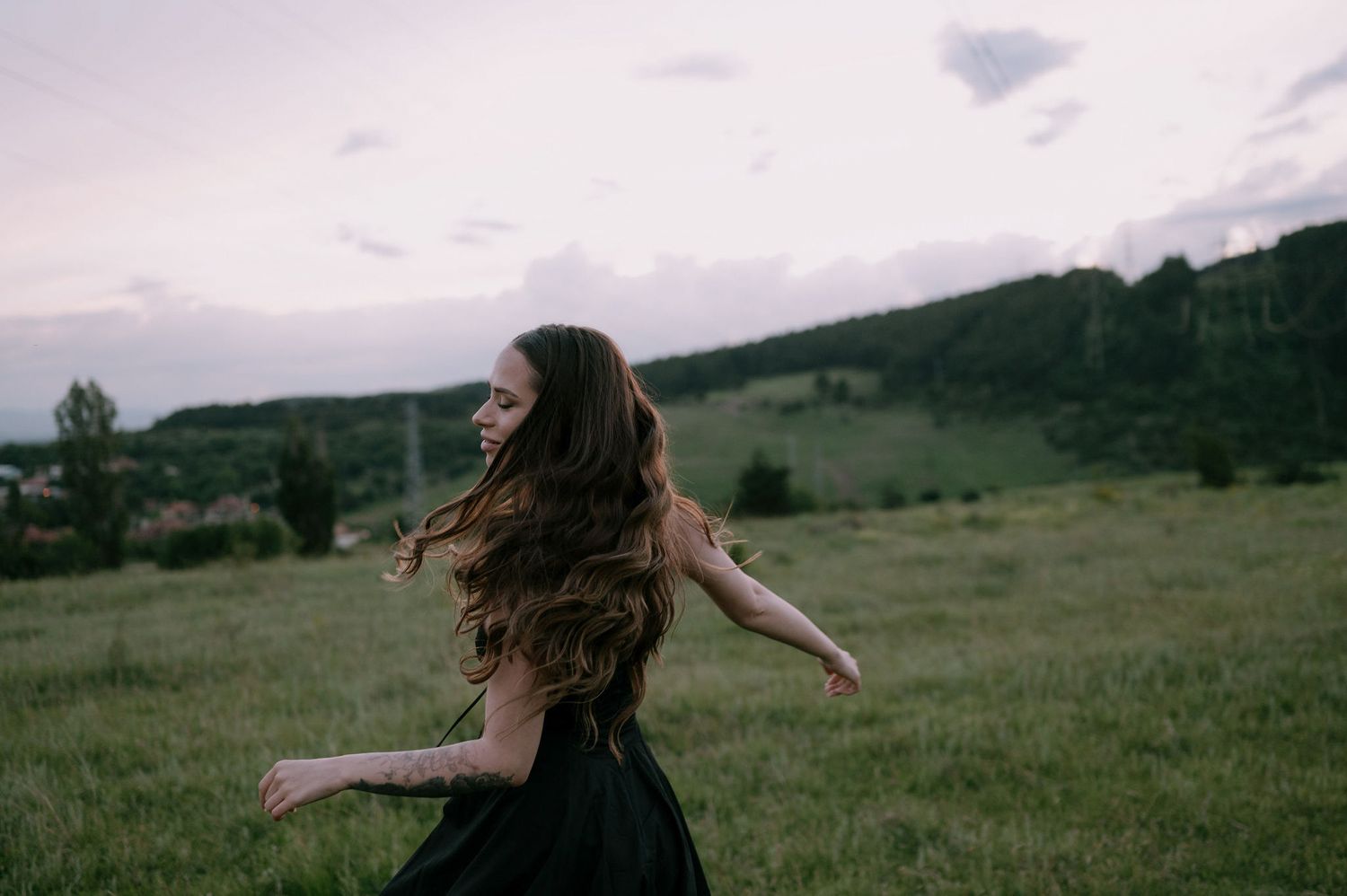Panoramic sequence of a person with flowing hair spinning joyfully in a green mountain meadow at sunset.