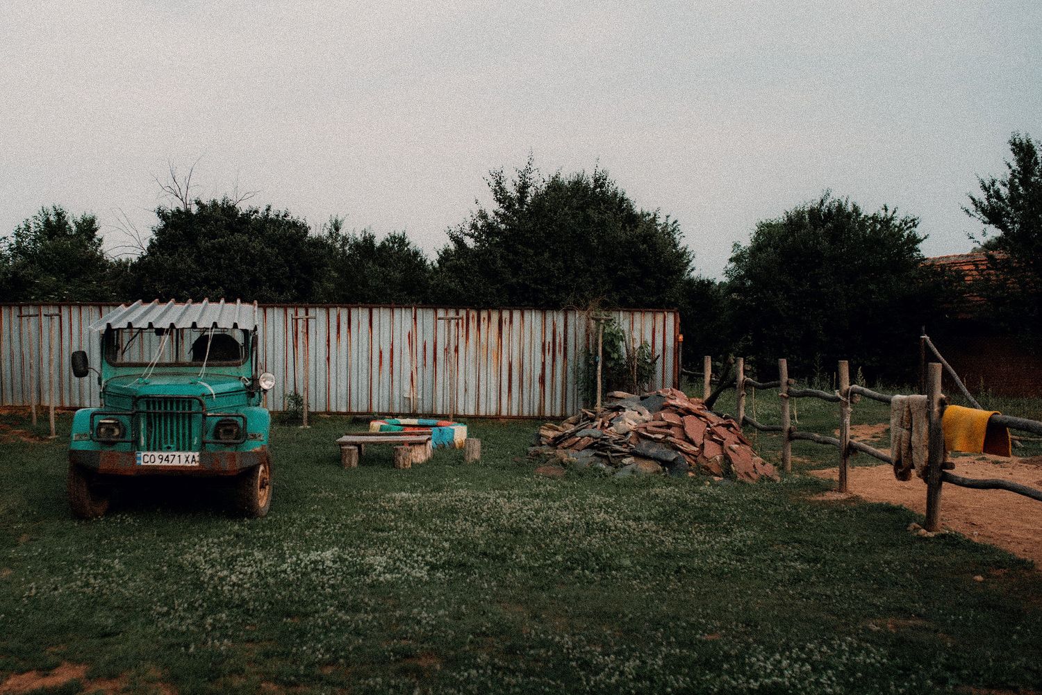 A panoramic view of rustic shipping containers and industrial equipment scattered across a grassy rural landscape.