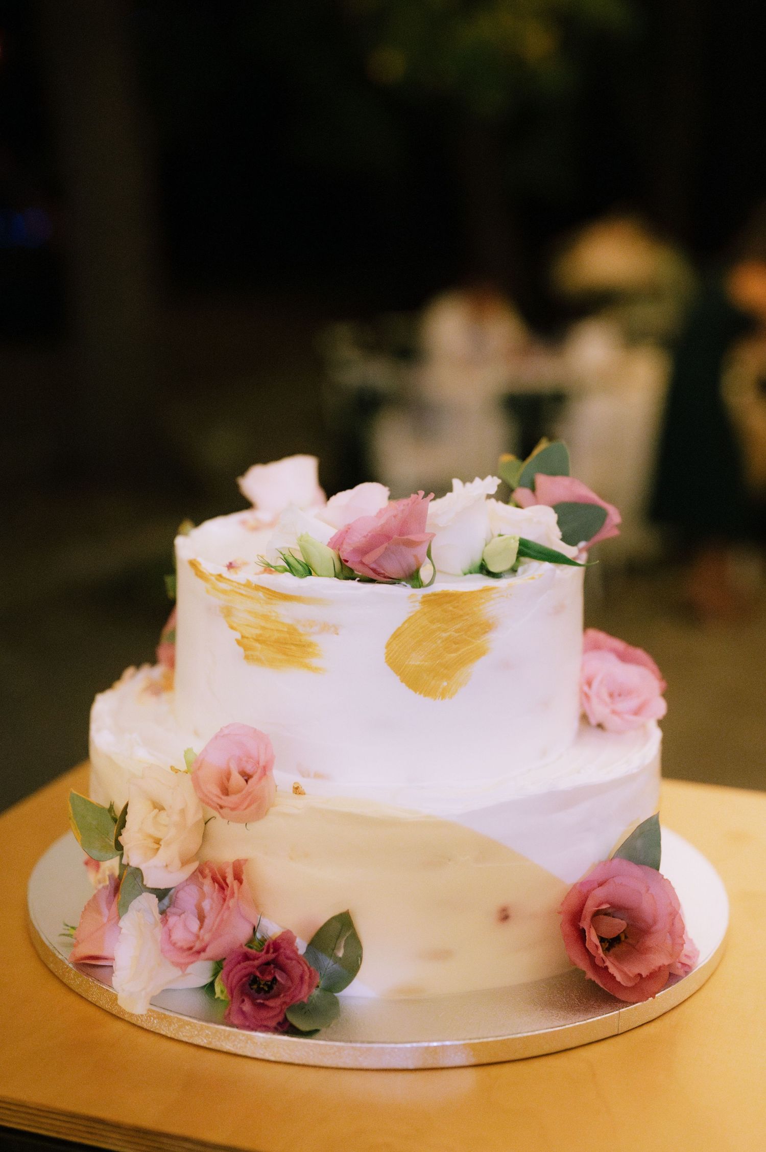 A white frosted cake decorated with delicate pink roses and eucalyptus leaves displayed from multiple angles.