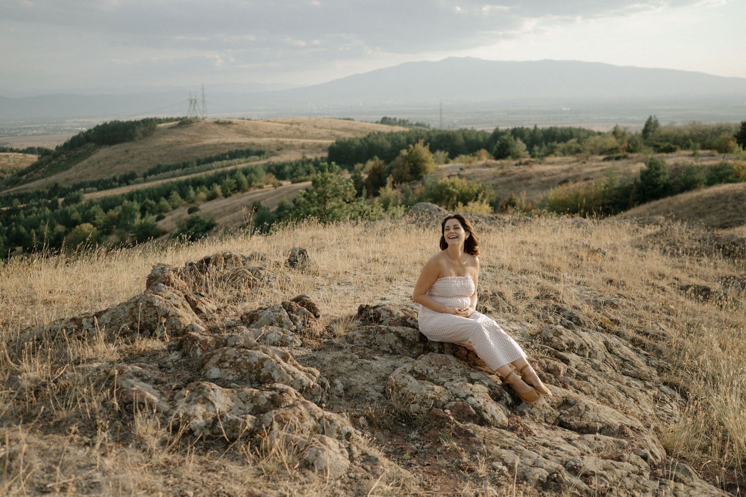 Person in white dress poses on scenic California hillside during golden hour sunset photography session.