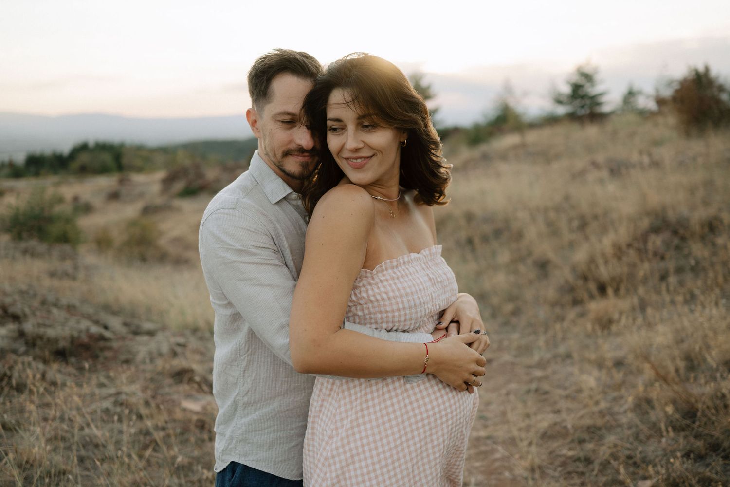 A couple embraces on a scenic hillside during a romantic outdoor photoshoot at golden hour.