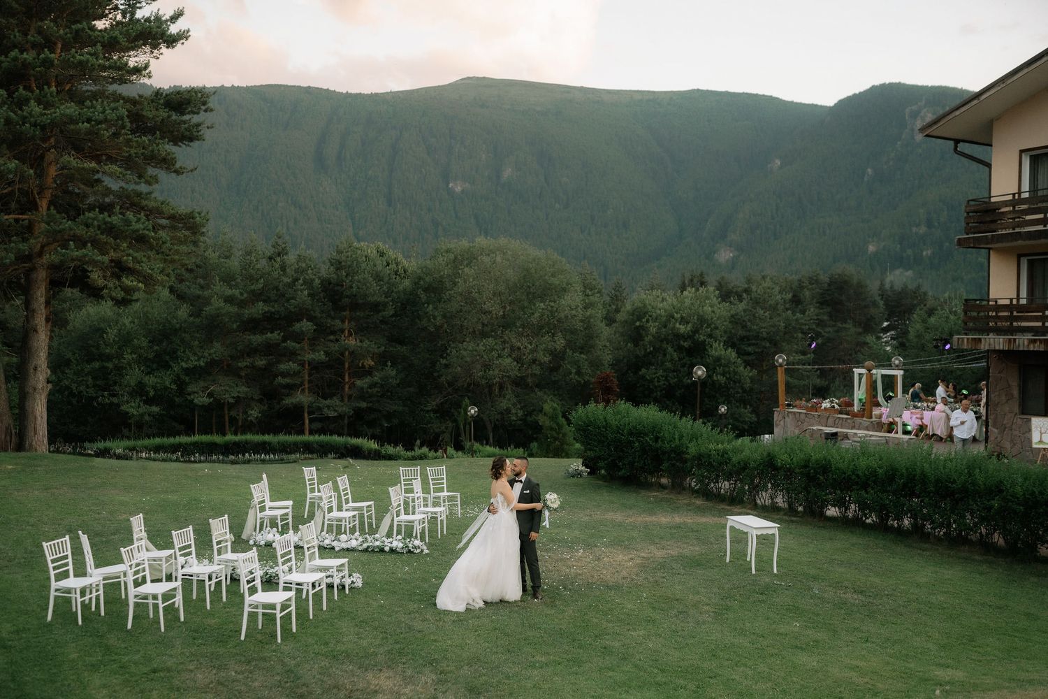 A scenic outdoor wedding ceremony setup with white chairs on a lawn overlooking mountain views at a rustic venue.