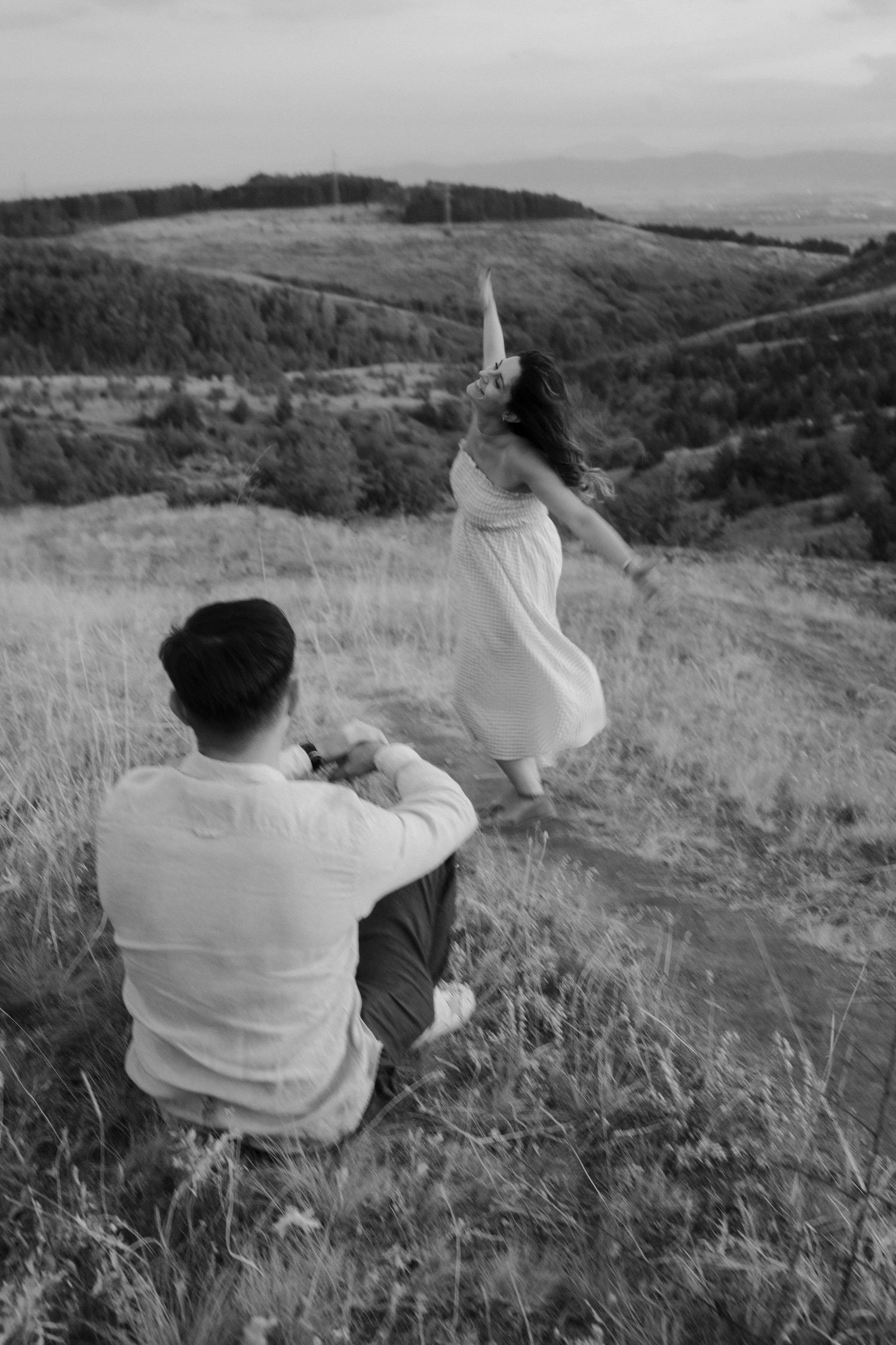 A series of black and white photographs showing someone in a white shirt sitting on a grassy hillside overlooking a landscape.
