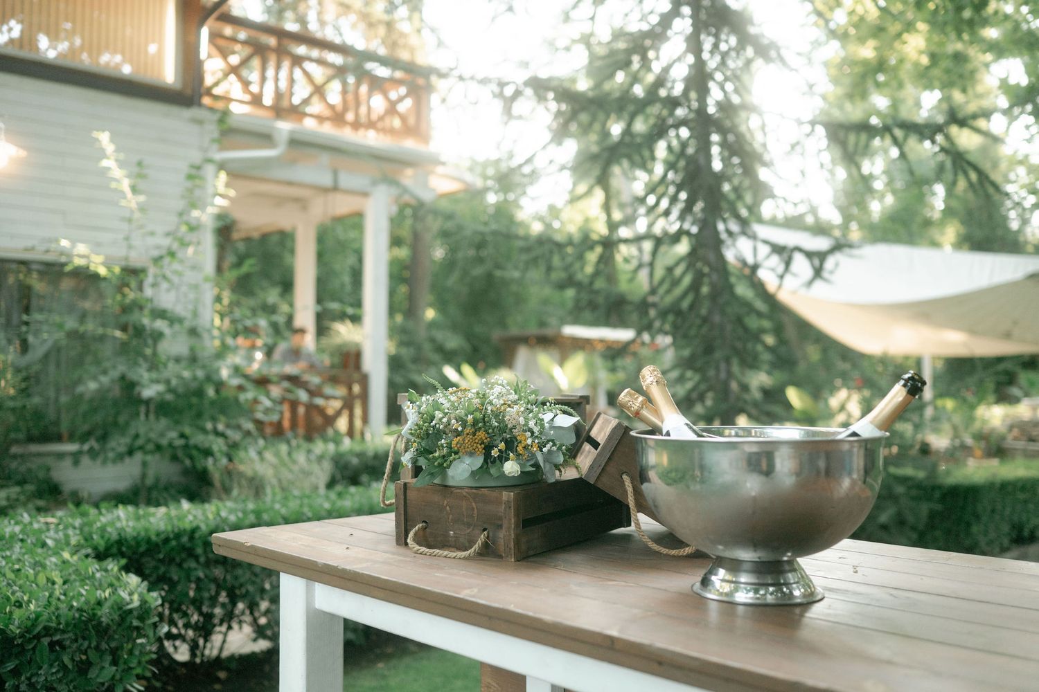 Rustic wooden deck with outdoor furniture and decorative metal bowls surrounded by lush green trees and foliage.