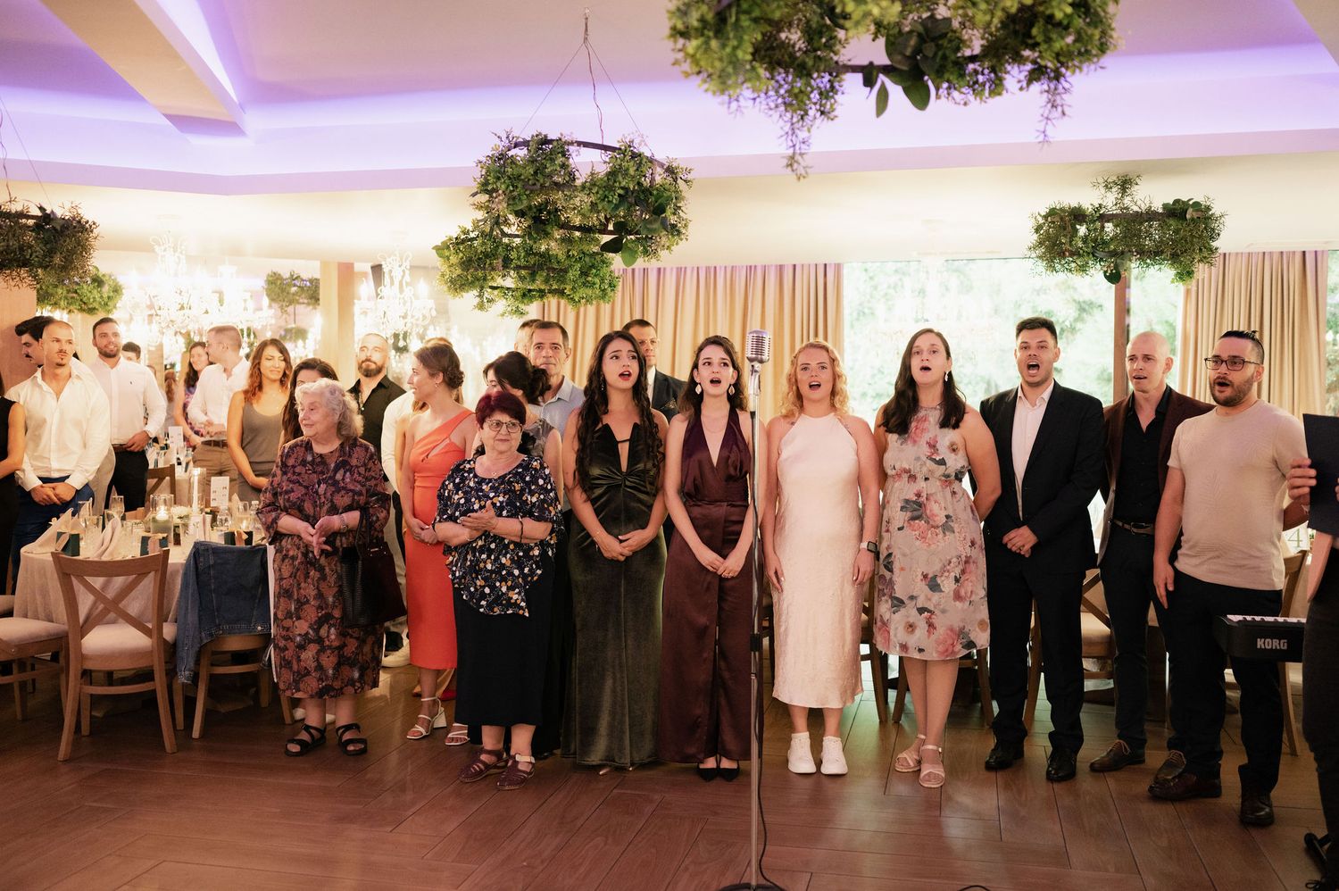 Wedding guests stand in line during a reception ceremony in an elegant ballroom with purple lighting and decorative trees.