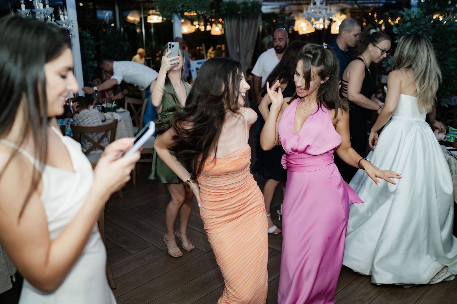 A group of wedding guests dance together on a dark dance floor during an evening reception celebration.