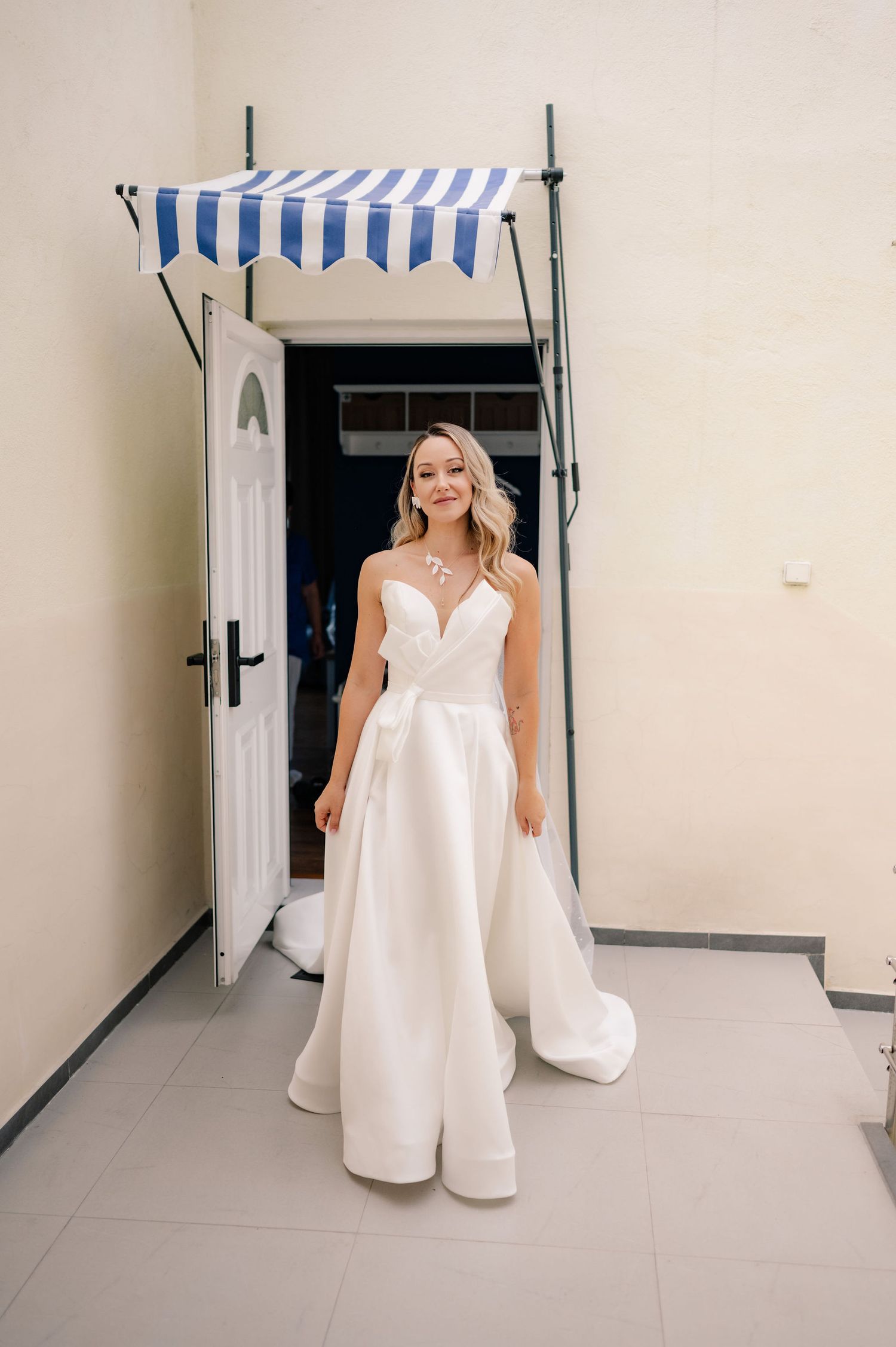 A person in a flowing white wedding dress poses in a hallway with blue and white striped awning decorations.