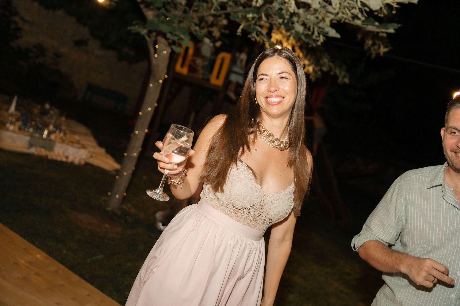 A group celebrates at an outdoor evening event with string lights creating a warm, festive atmosphere.