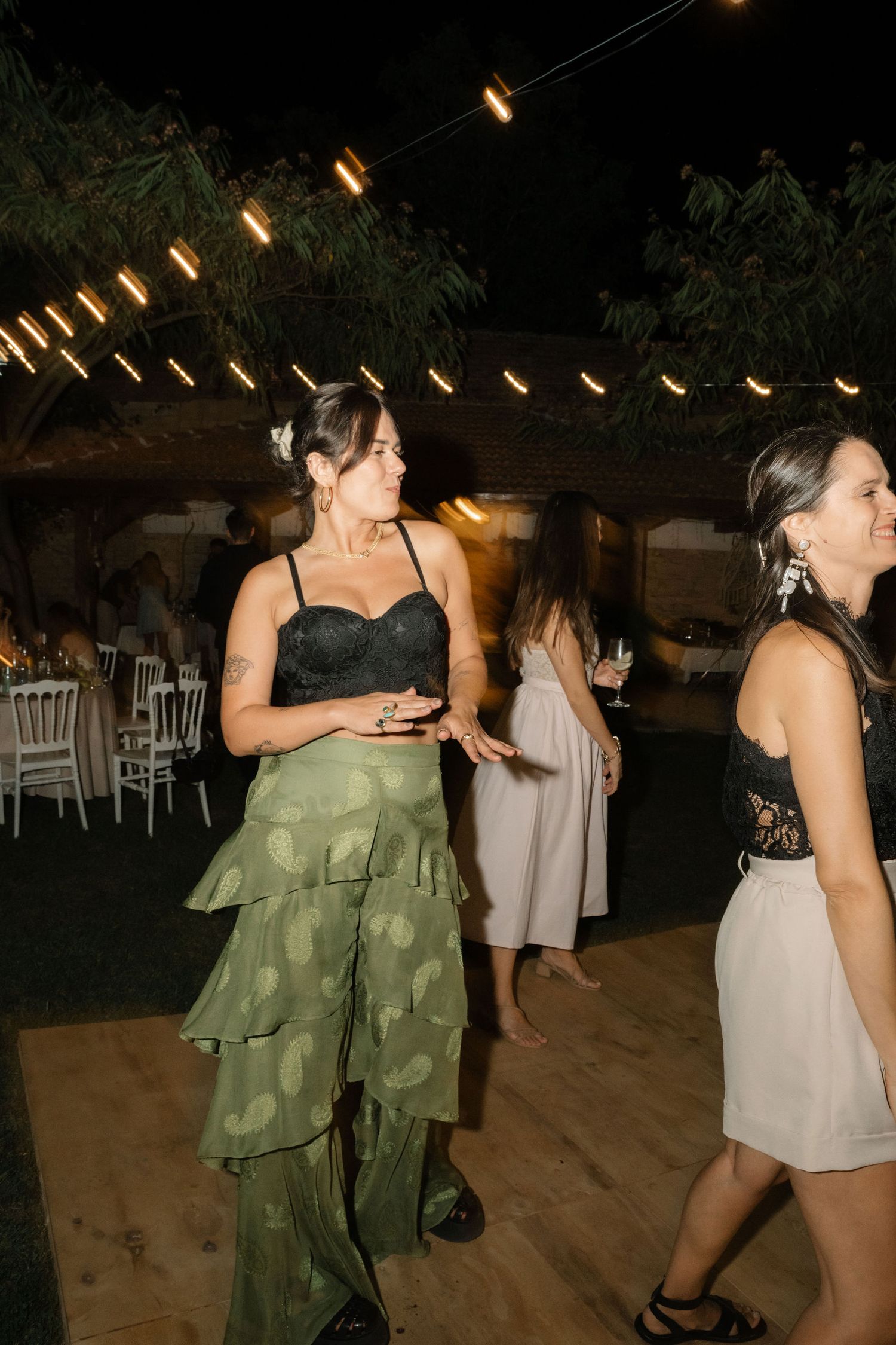 People dancing at an outdoor evening event with string lights illuminating the dance floor.