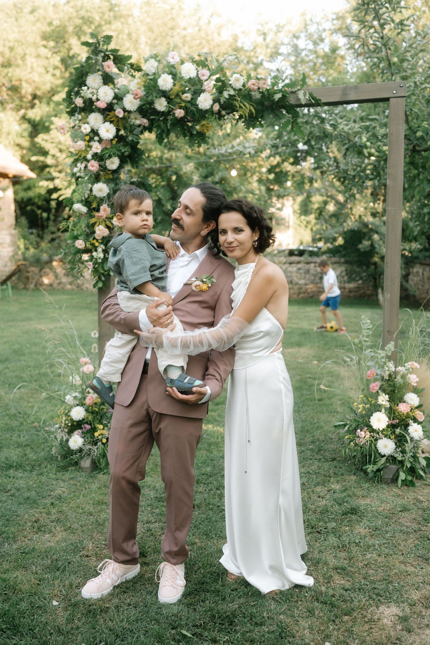 A tender family moment captured in a garden setting with white roses and greenery on a summer day.