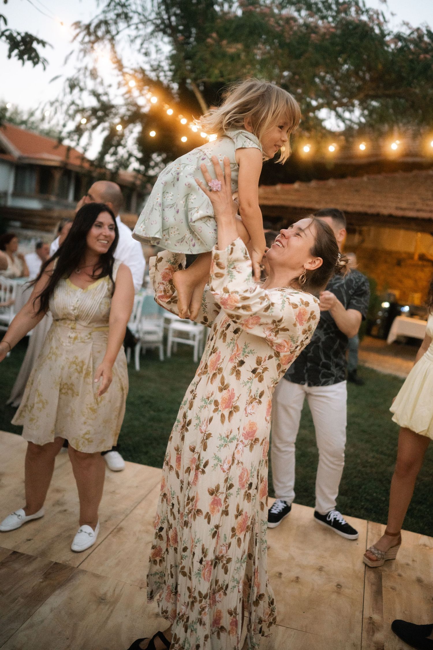 Couples dancing and embracing on an outdoor dance floor at dusk with string lights overhead.